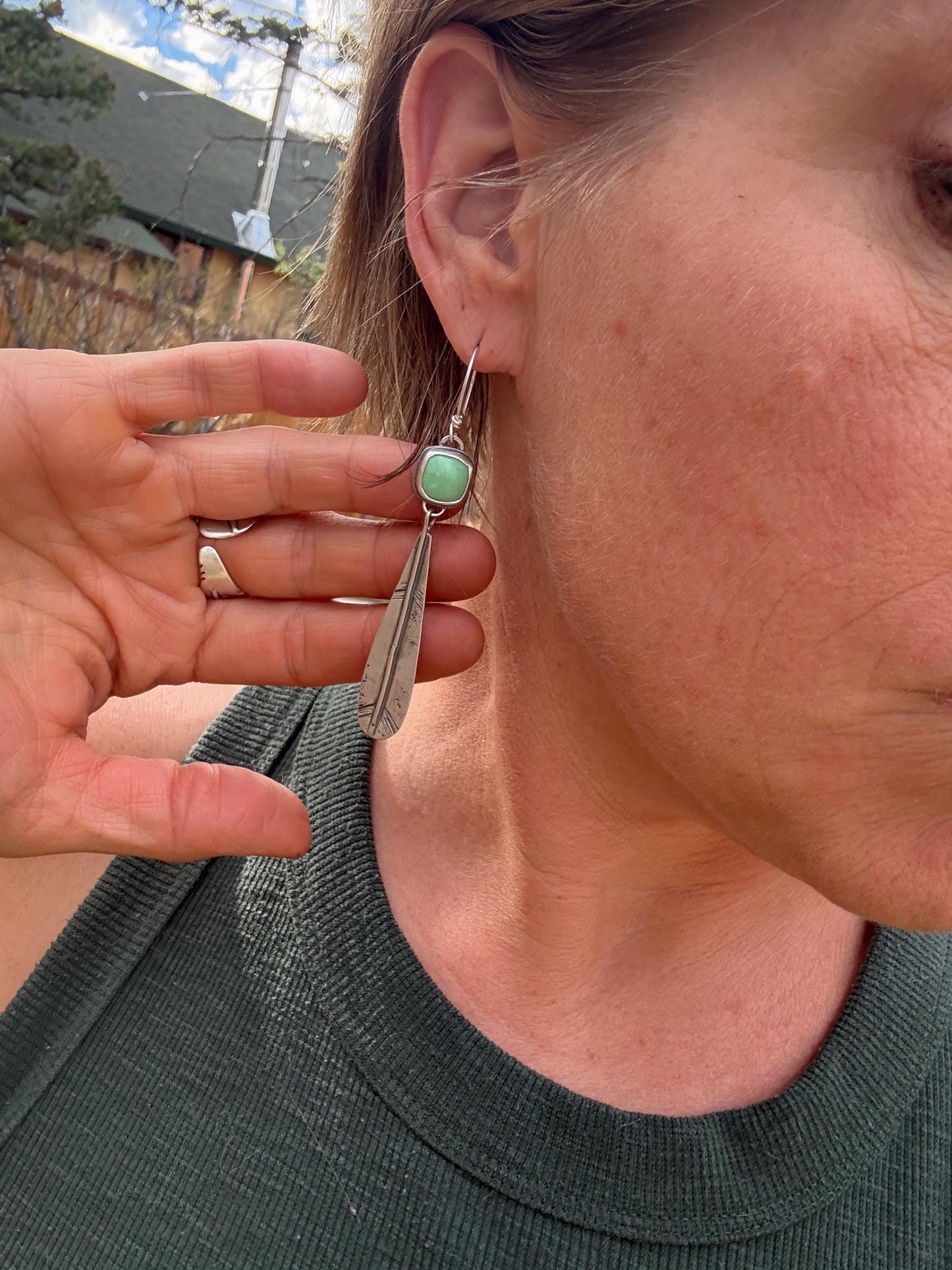 Close-up of a person wearing a silver earring with a green gemstone, held up to the ear.