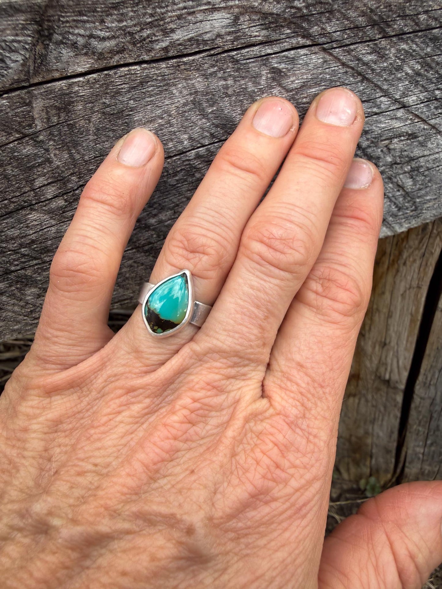Hand wearing a ring with a green stone on a wooden surface
