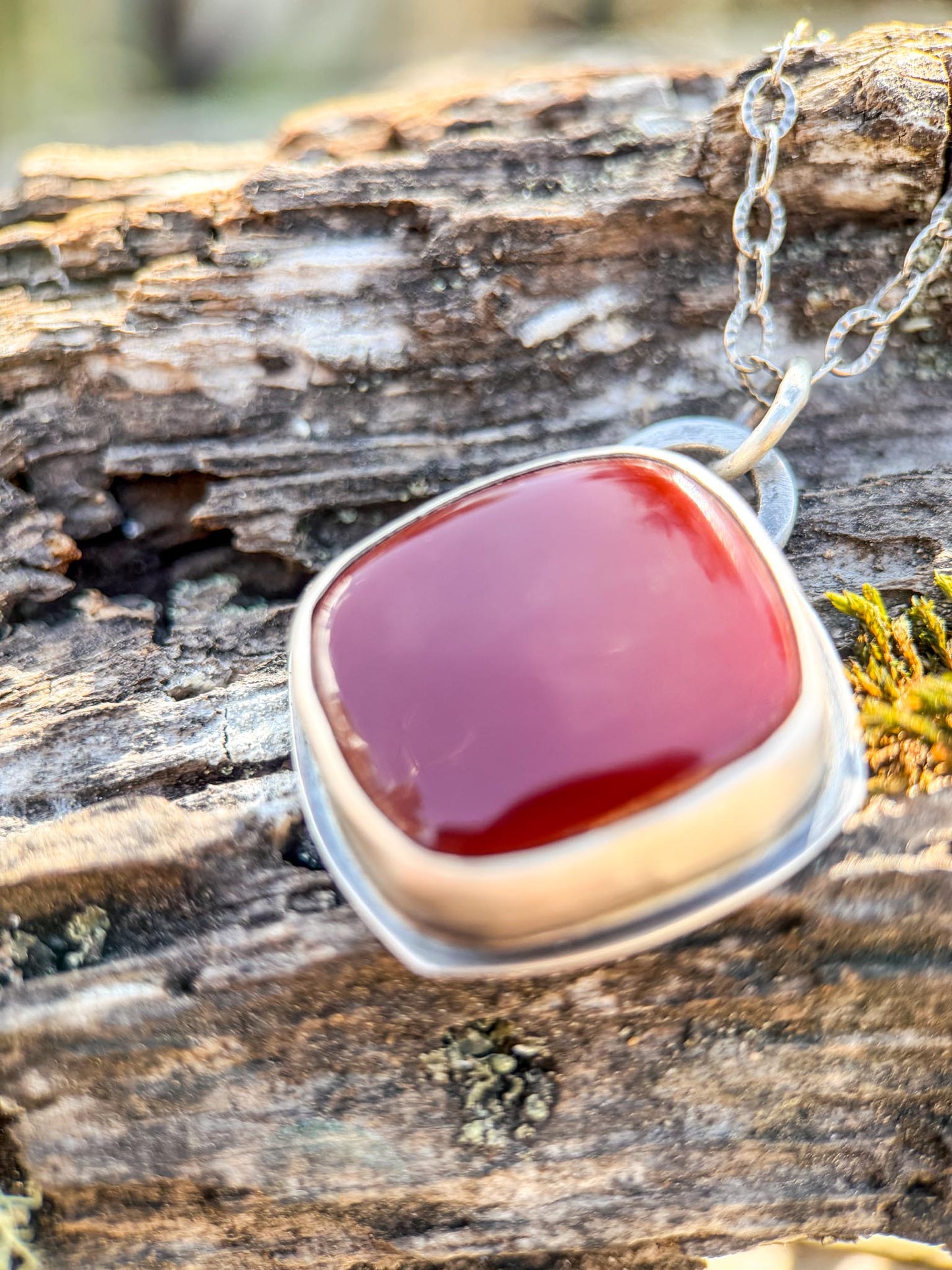 Red stone pendant on a silver chain resting on a wooden surface