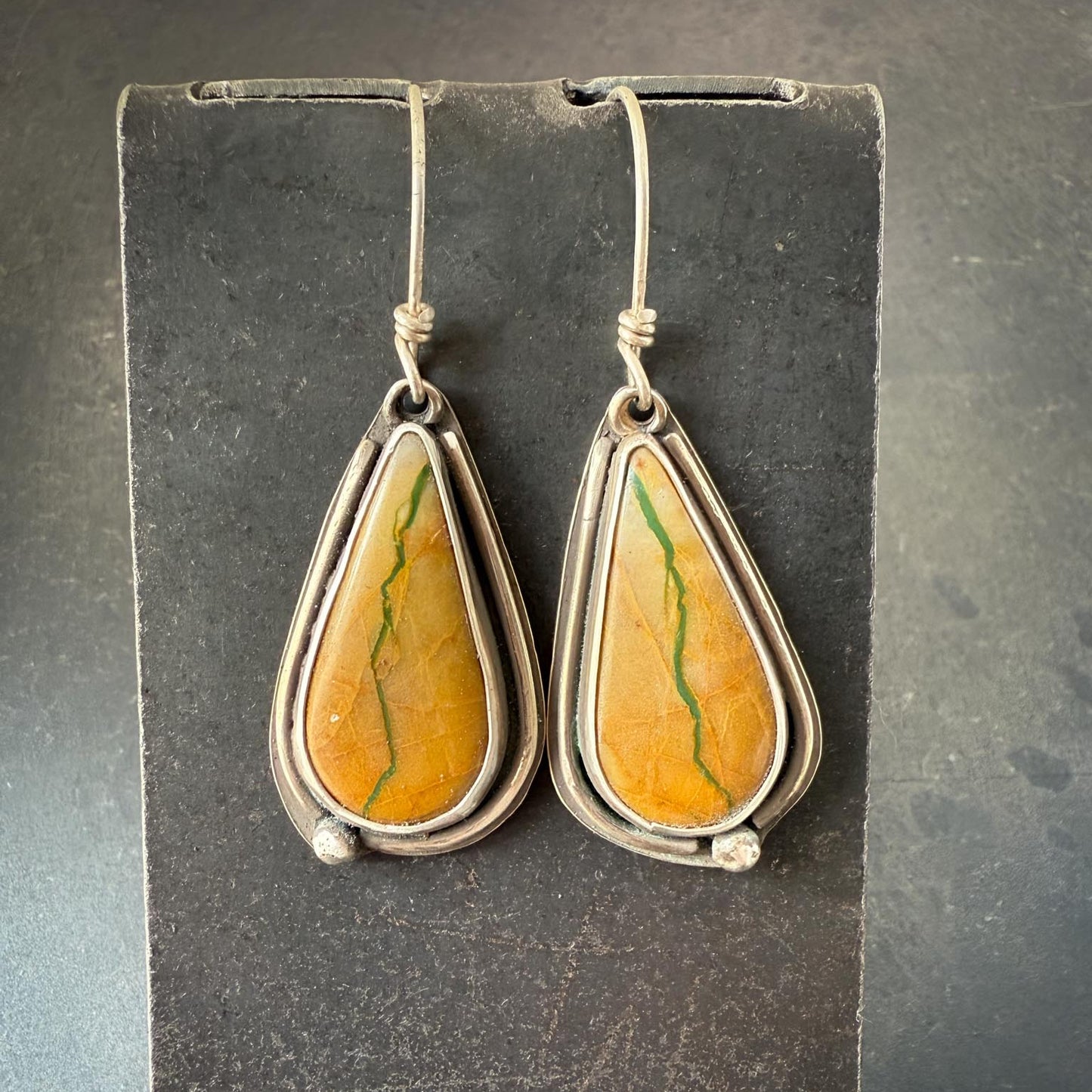Teardrop-shaped Royston turquoise earrings. Stones have yellow hue with interesting matrix and a deep turquoise vein running from top to bottom, resembling a river, and silver settings on a dark gray background