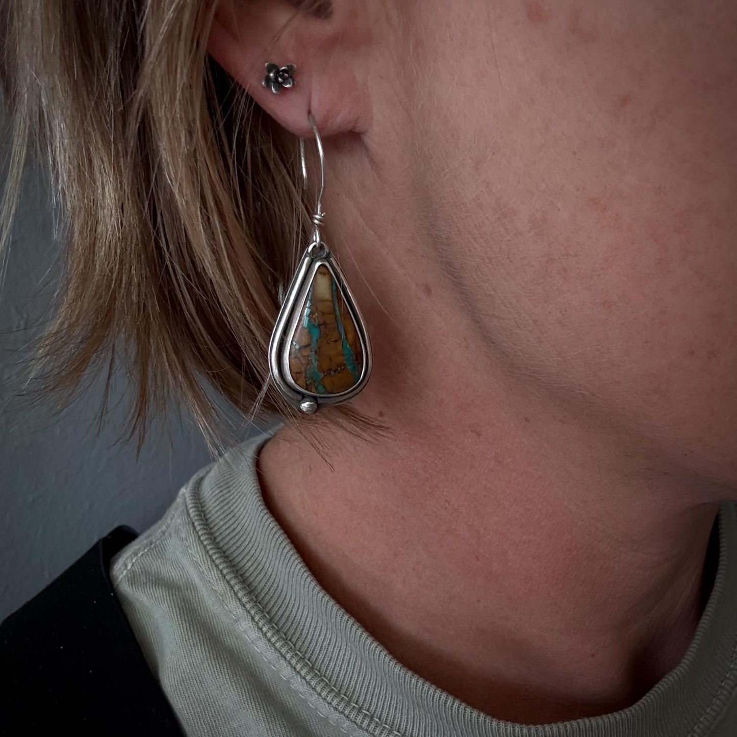 Close-up of a person wearing a silver earring with a green stone.