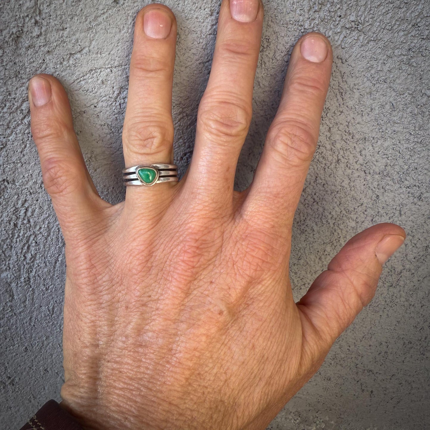 Hand wearing a silver ring with a green gemstone on a textured gray background