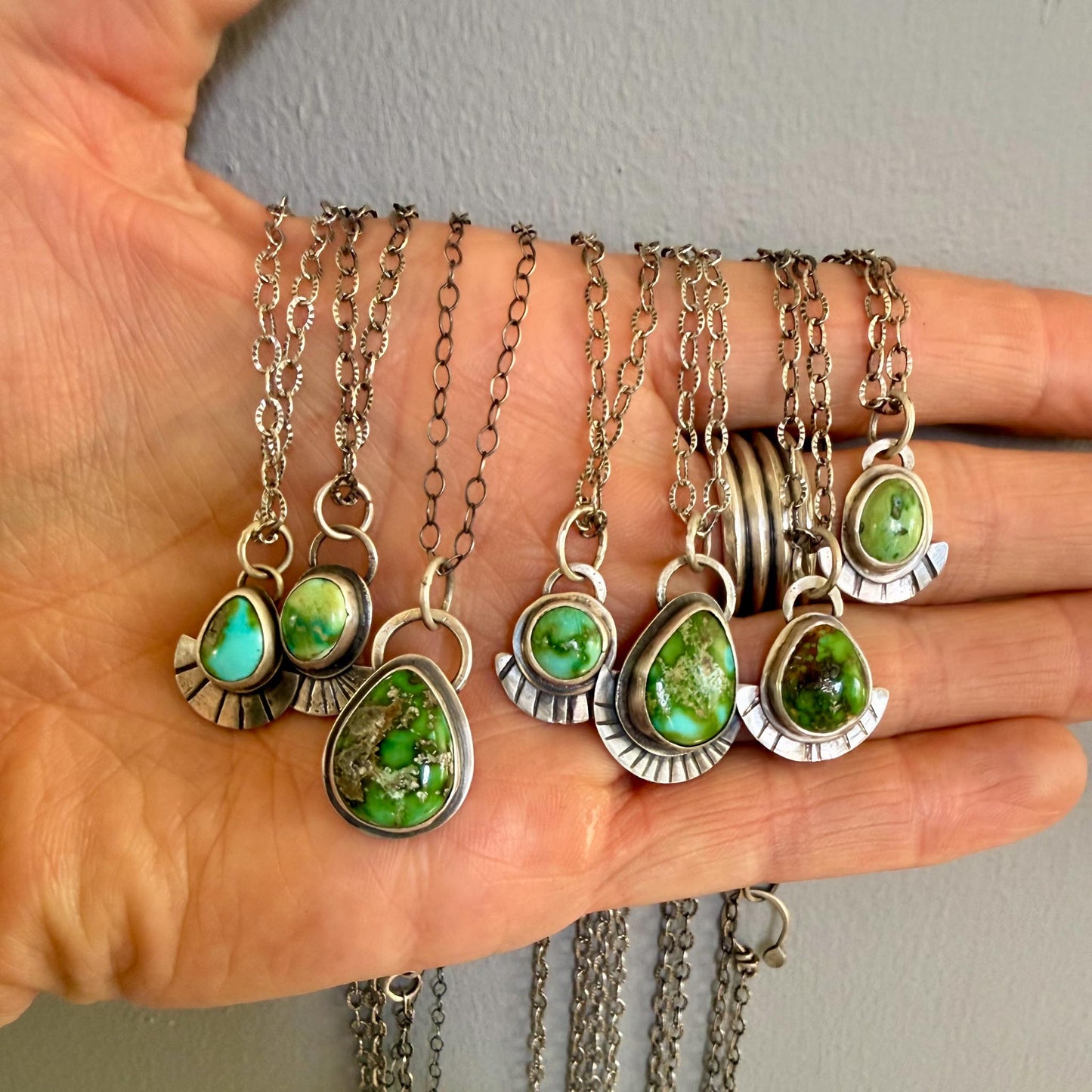 Hand holding multiple silver necklaces with green stone pendants against a neutral background