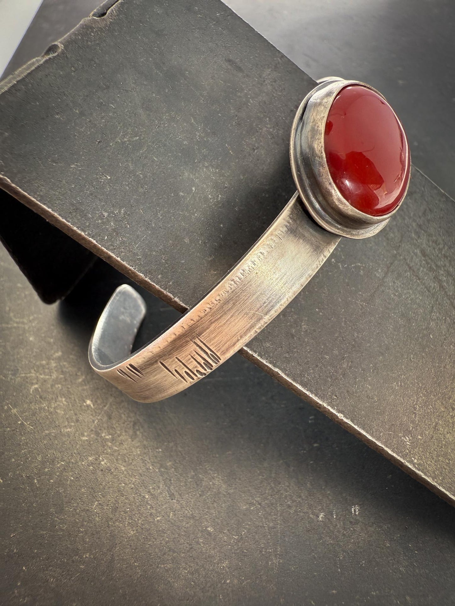 Silver bracelet with a red stone on a dark surface