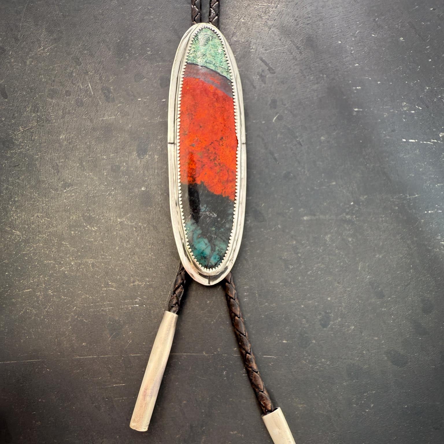 Bolo tie with colorful oval design on a dark surface