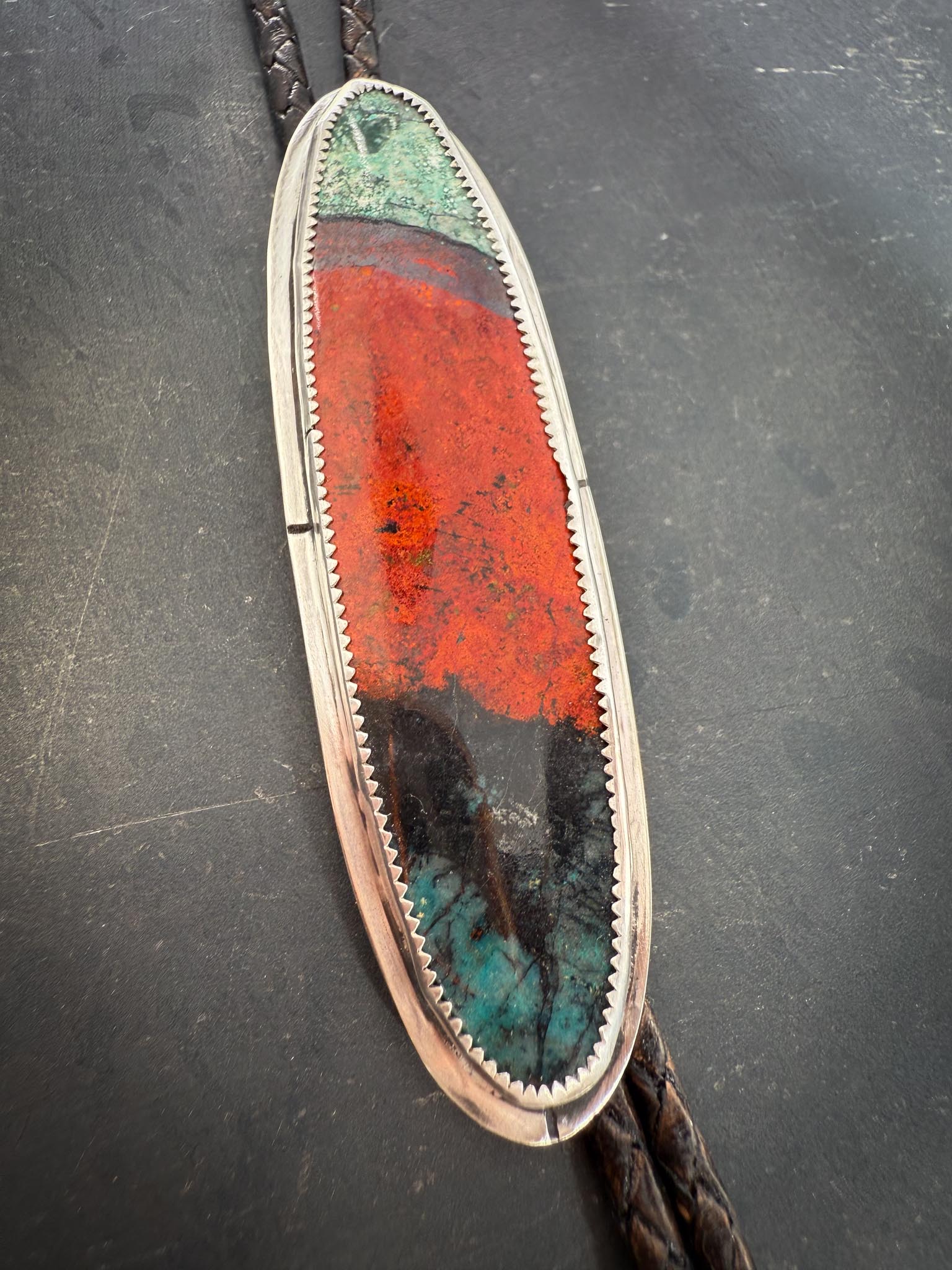 Bolo tie with multicolored stone and leather strap on a dark background
