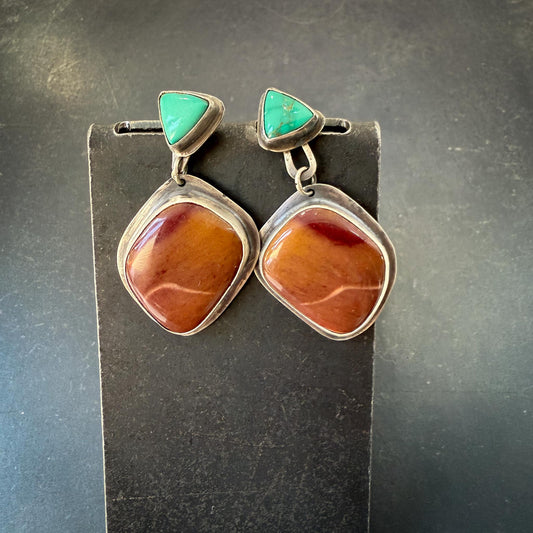 Pair of earrings with brown and green stones on a dark background