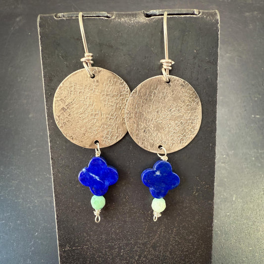 Pair of earrings with round metallic discs and blue clover-shaped beads on a dark background