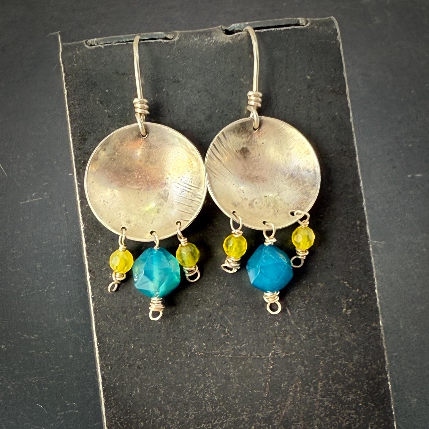 Silver earrings with blue and yellow beads on a black card