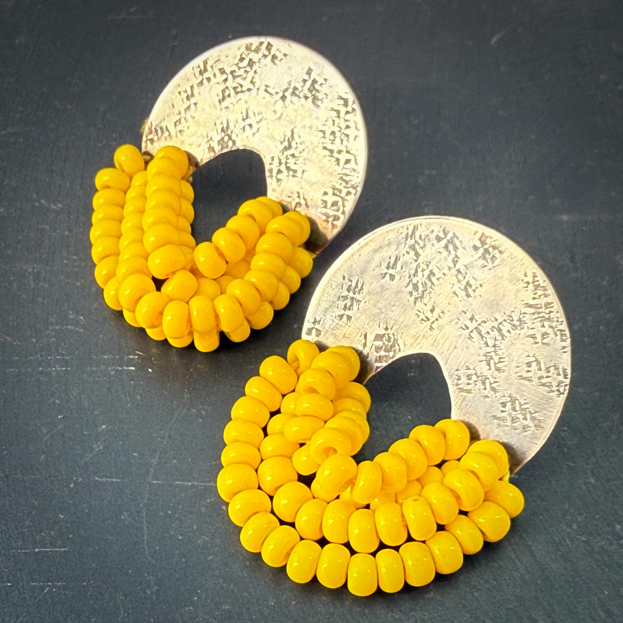 Yellow beaded earrings with silver circular backs on a dark surface