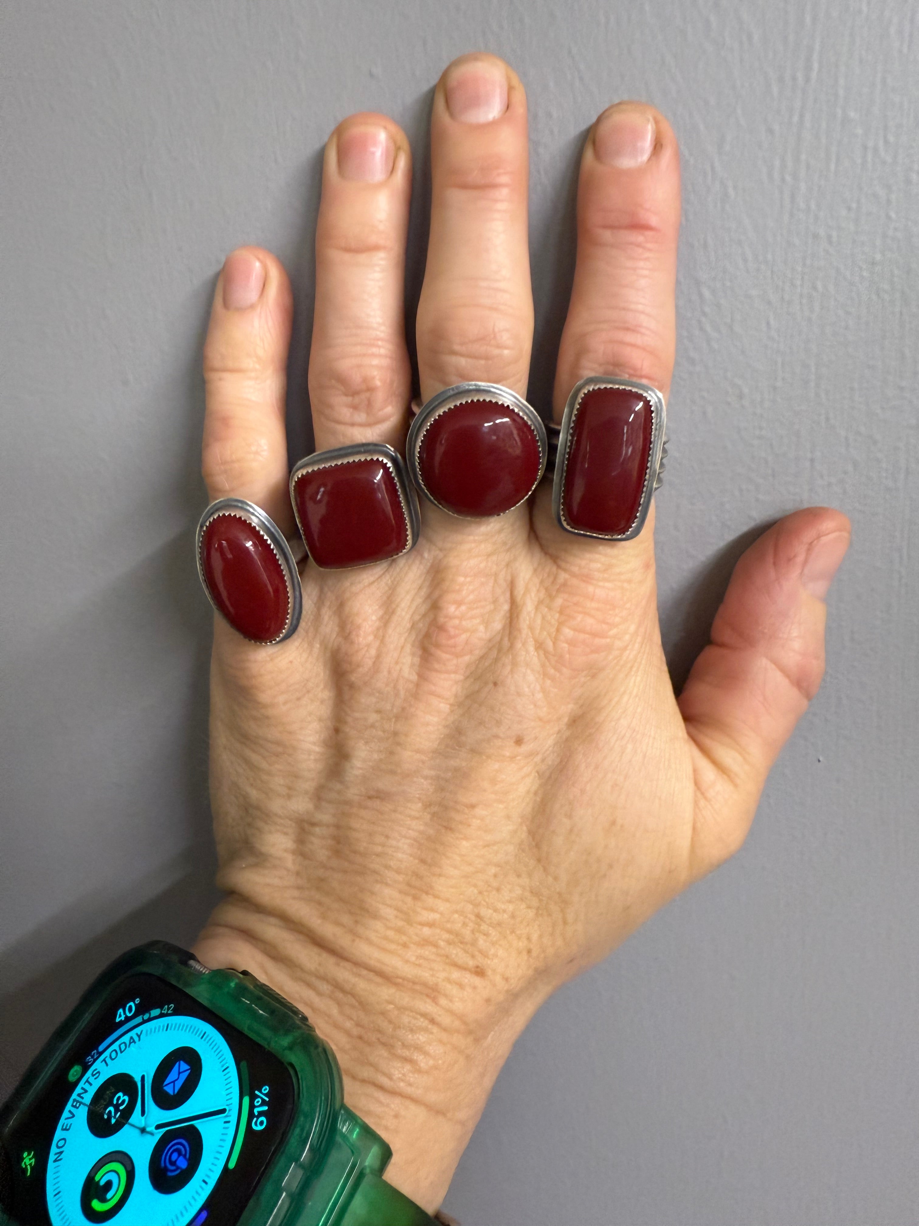 Hand wearing multiple red stone rings on a gray background