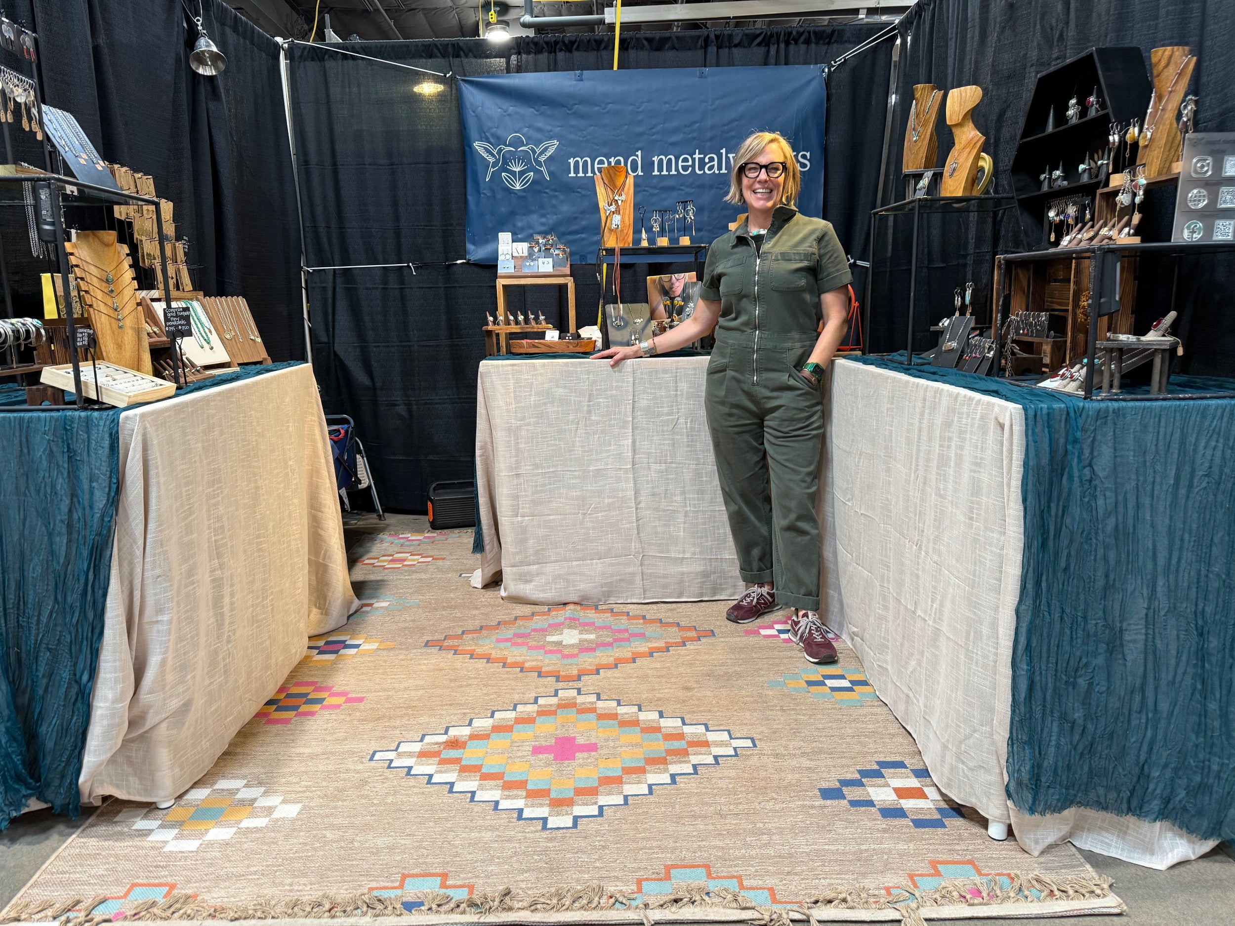 Woman standing behind a booth with wooden products at an event.
