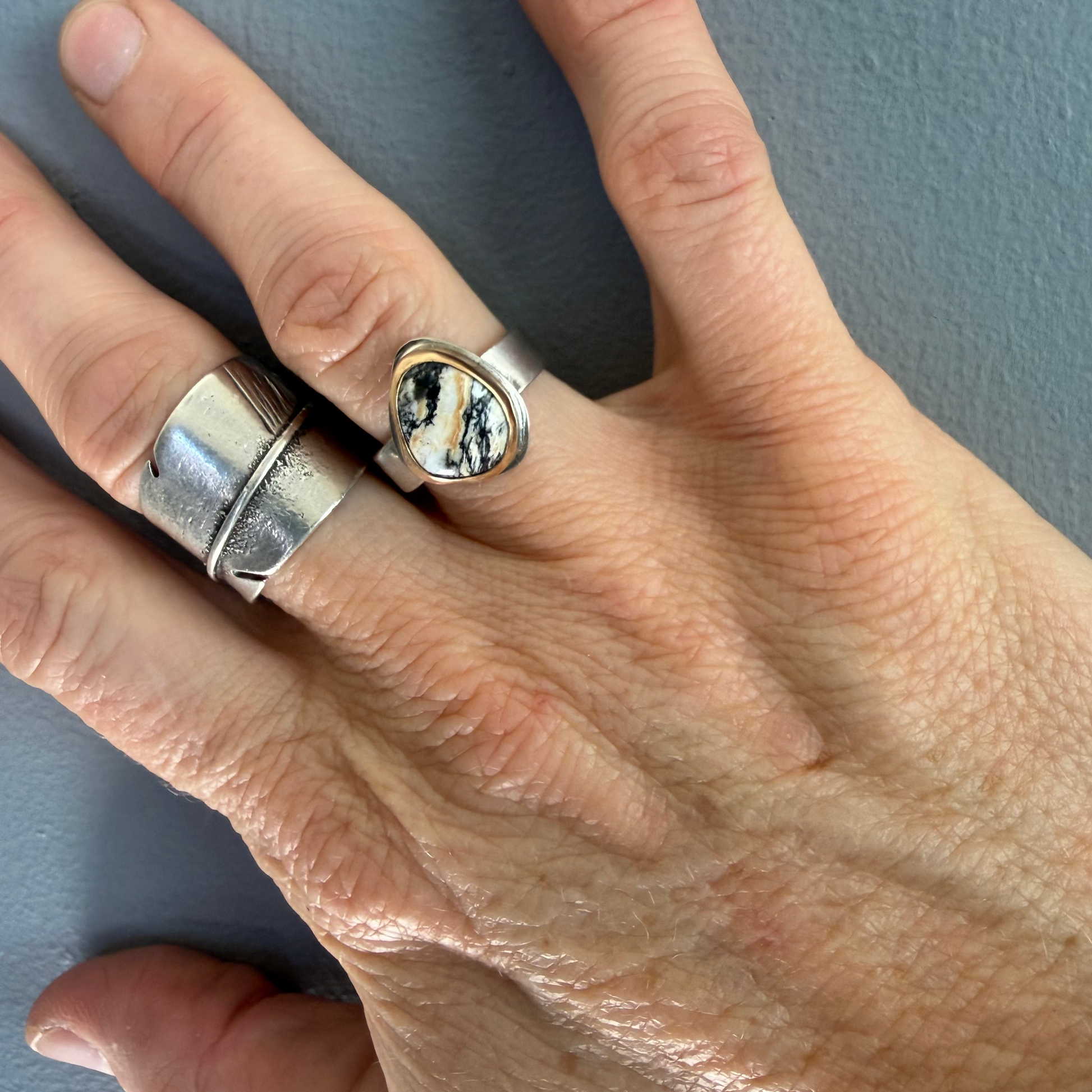 Hand wearing two silver rings on a gray background