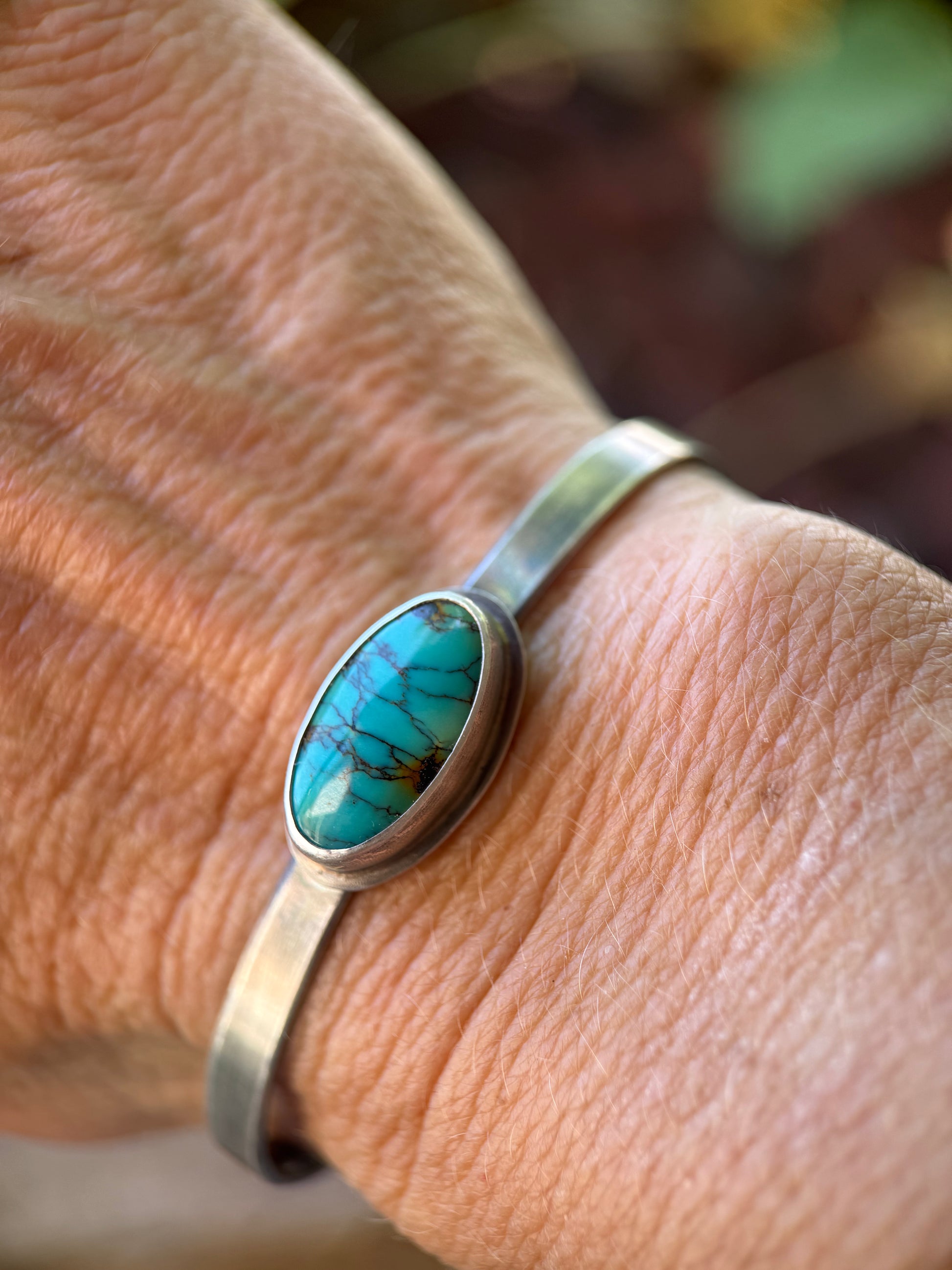 Silver bracelet with a turquoise stone on a wrist against a blurred natural background