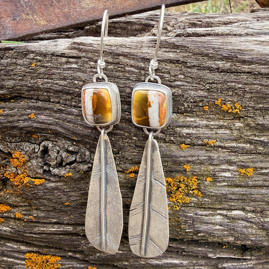 Silver feather earrings with polychrome turquoise stones on a wooden background