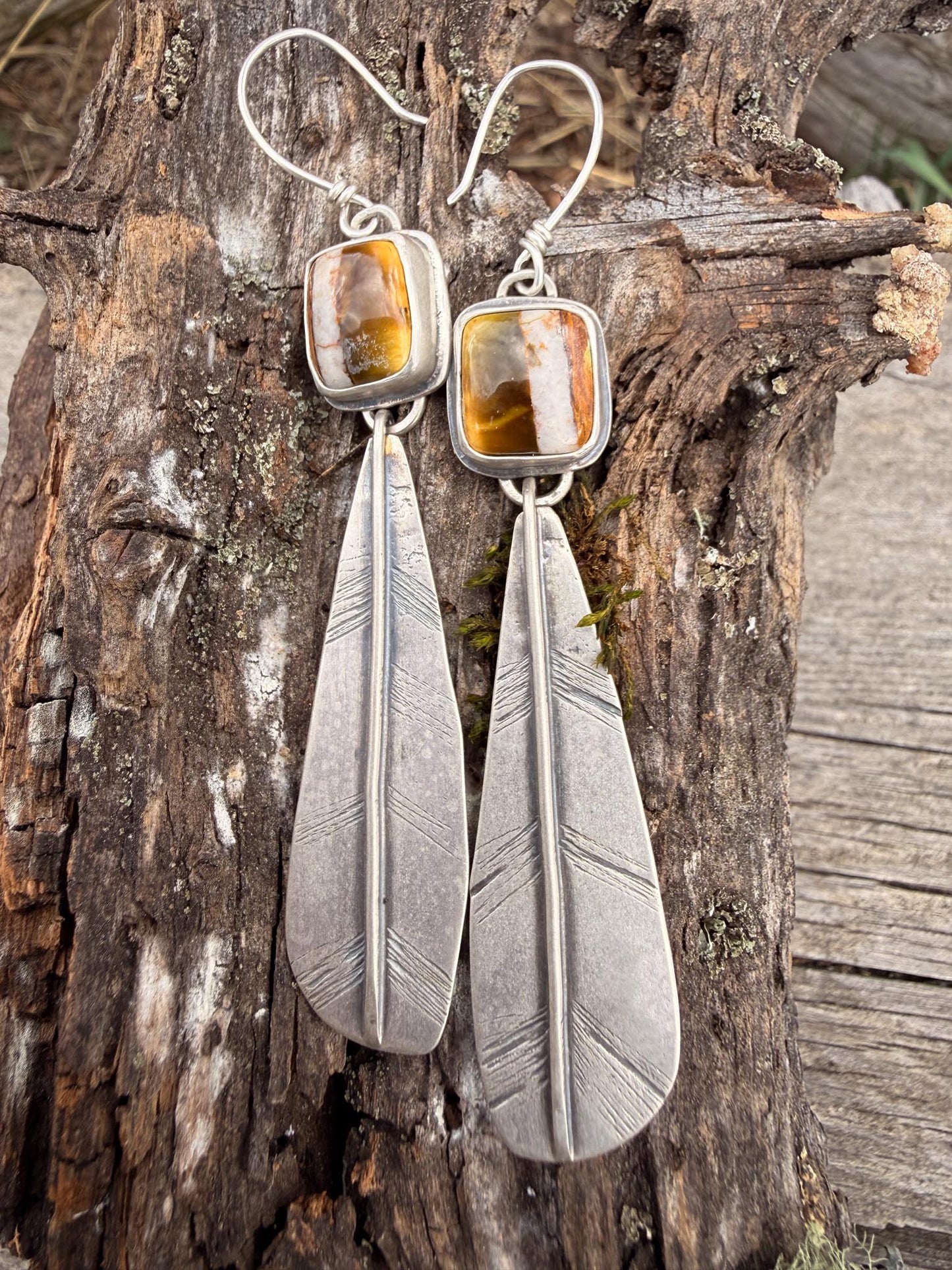Silver feather earrings with polychrome turquoise stones on a wooden background