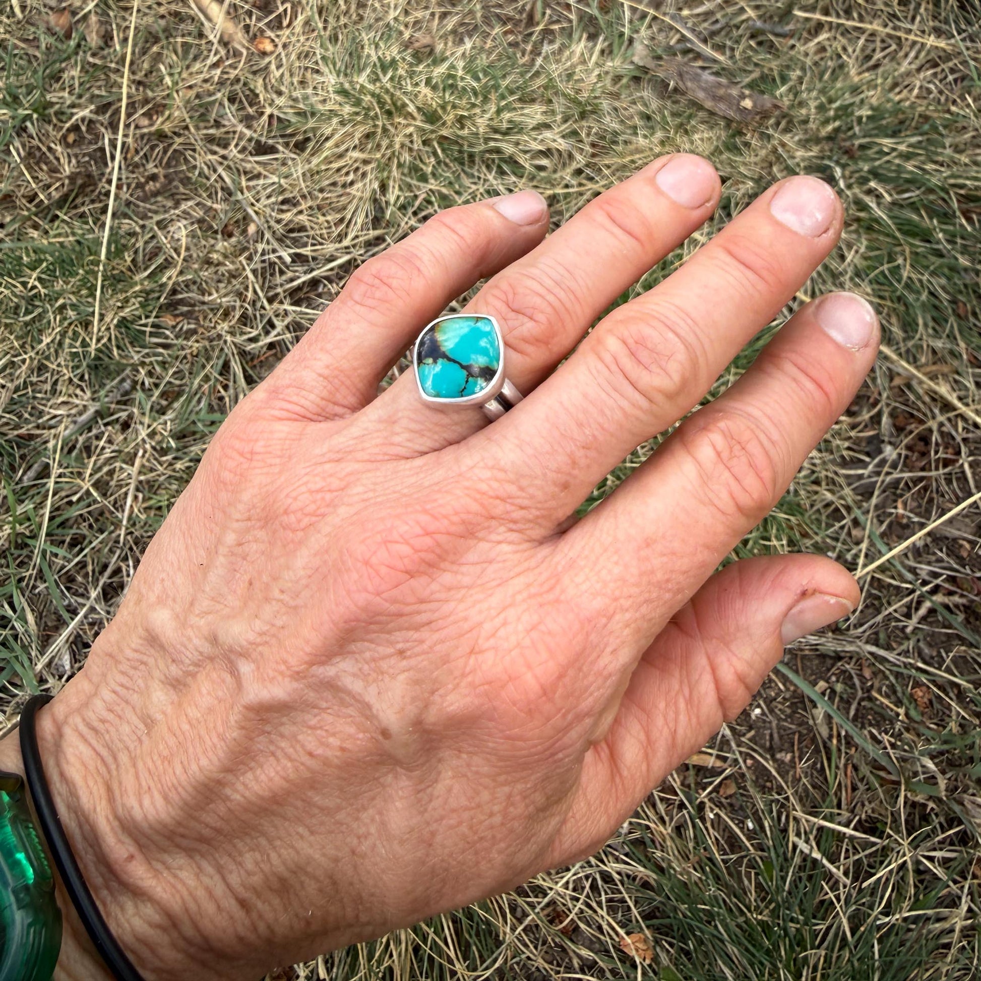Hand wearing a turquoise ring against a grassy background