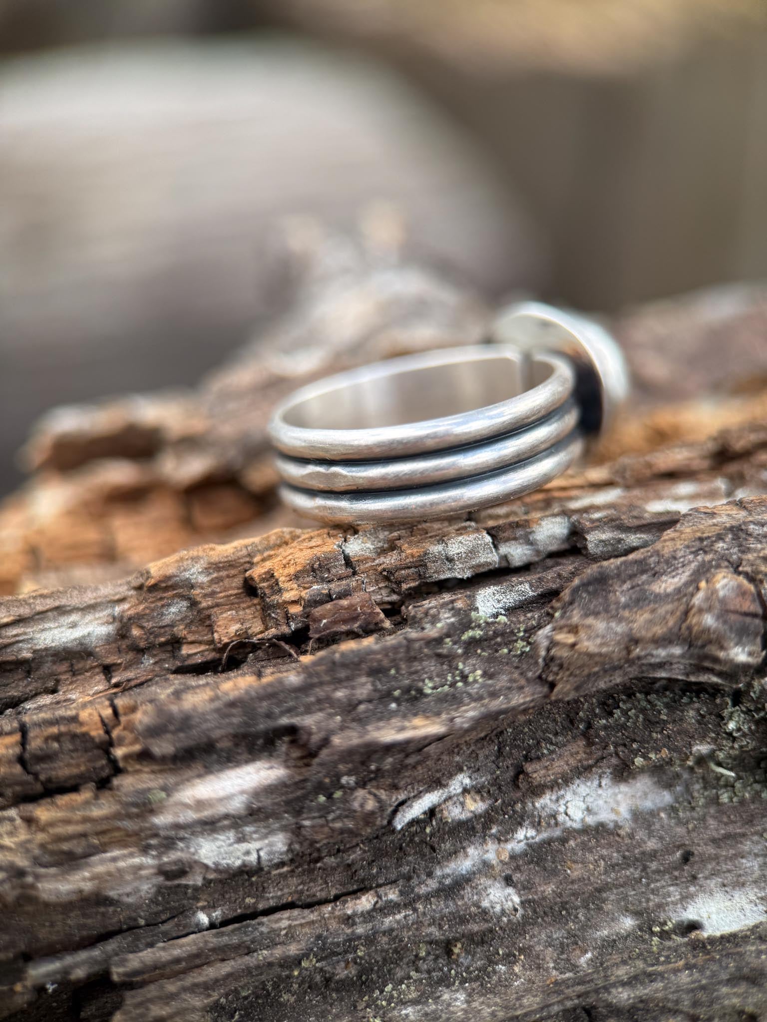 Stack of silver rings on a wooden surface with a blurred natural background