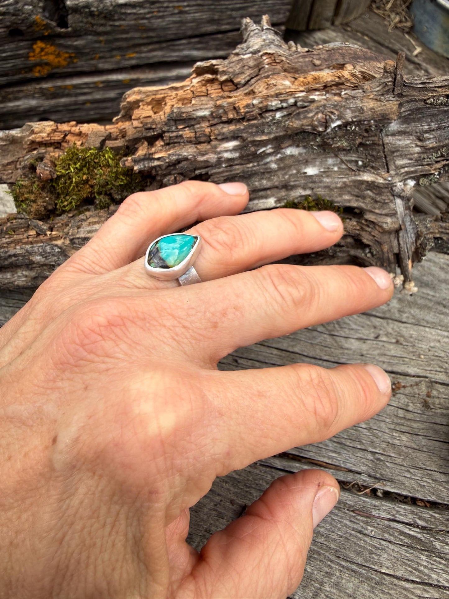 Hand wearing a ring with a turquoise stone on a wooden background