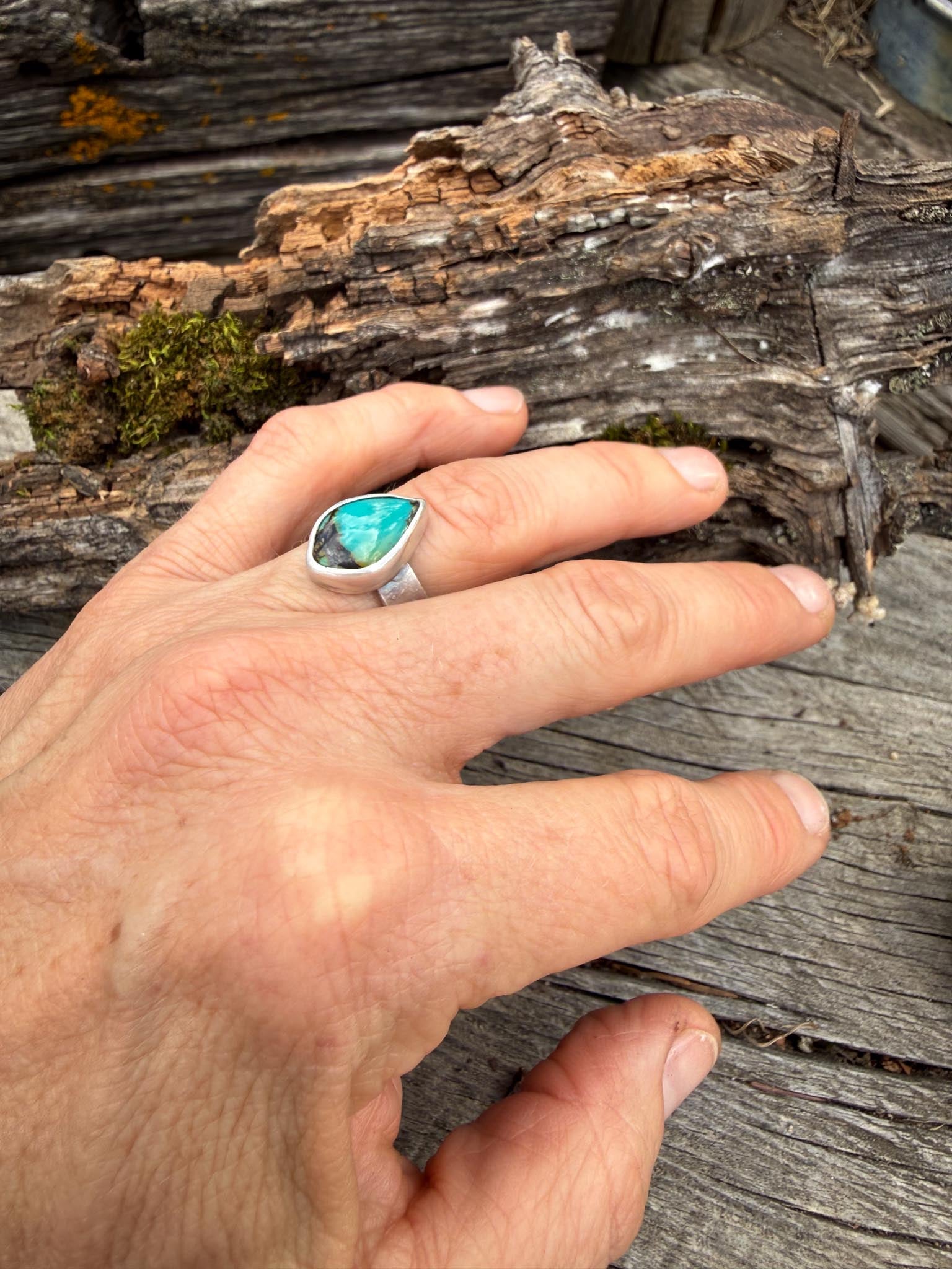 Hand wearing a ring with a turquoise stone on a wooden background