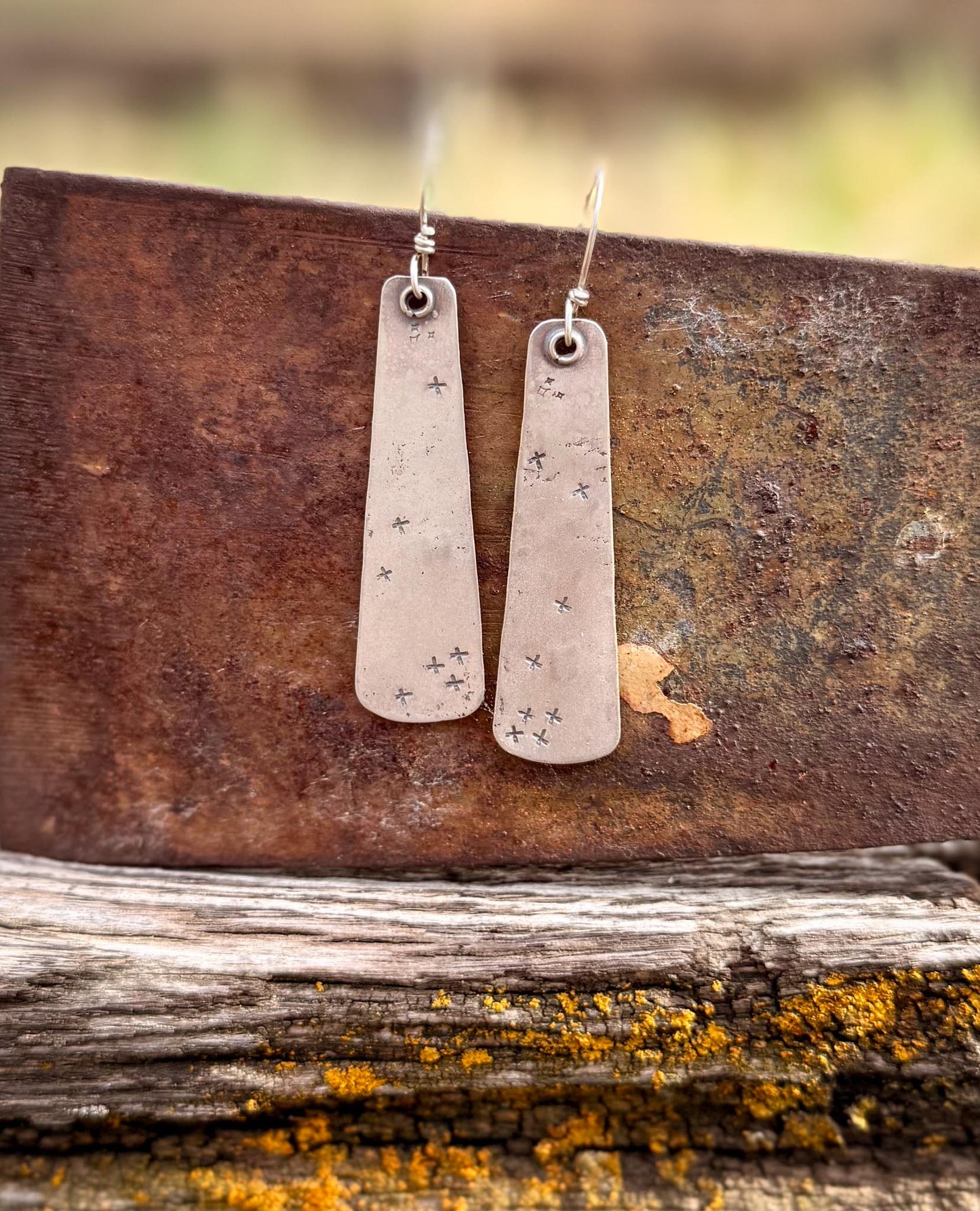 Pair of silver earrings on a rustic wooden surface with a blurred natural background
