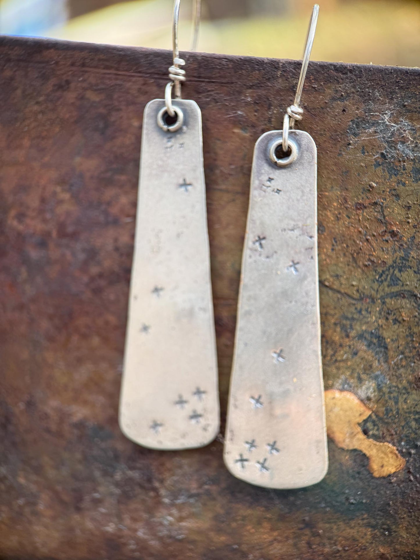 Pair of long, thin earrings with star patterns on a textured surface