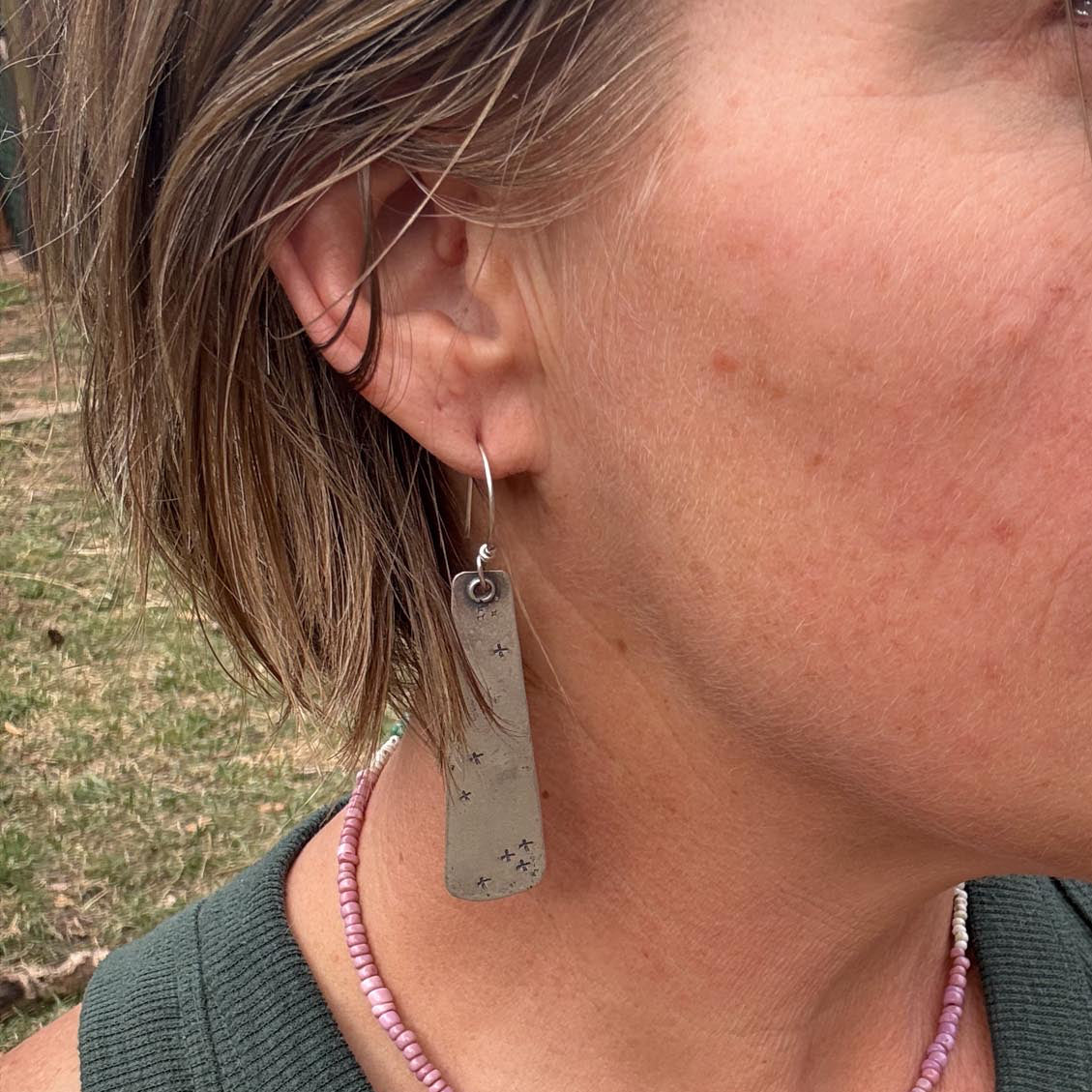Close-up of a person wearing earrings and a green sleeveless top with a blurred background