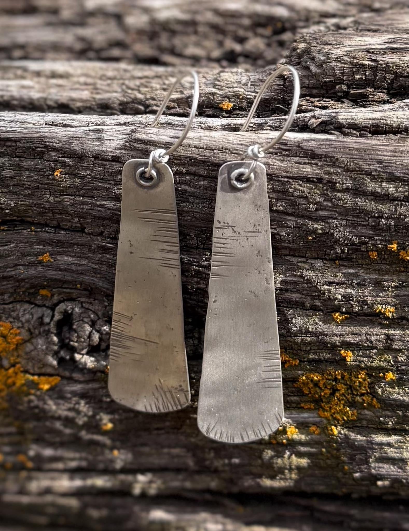 Pair of silver earrings on a wooden surface with lichen.