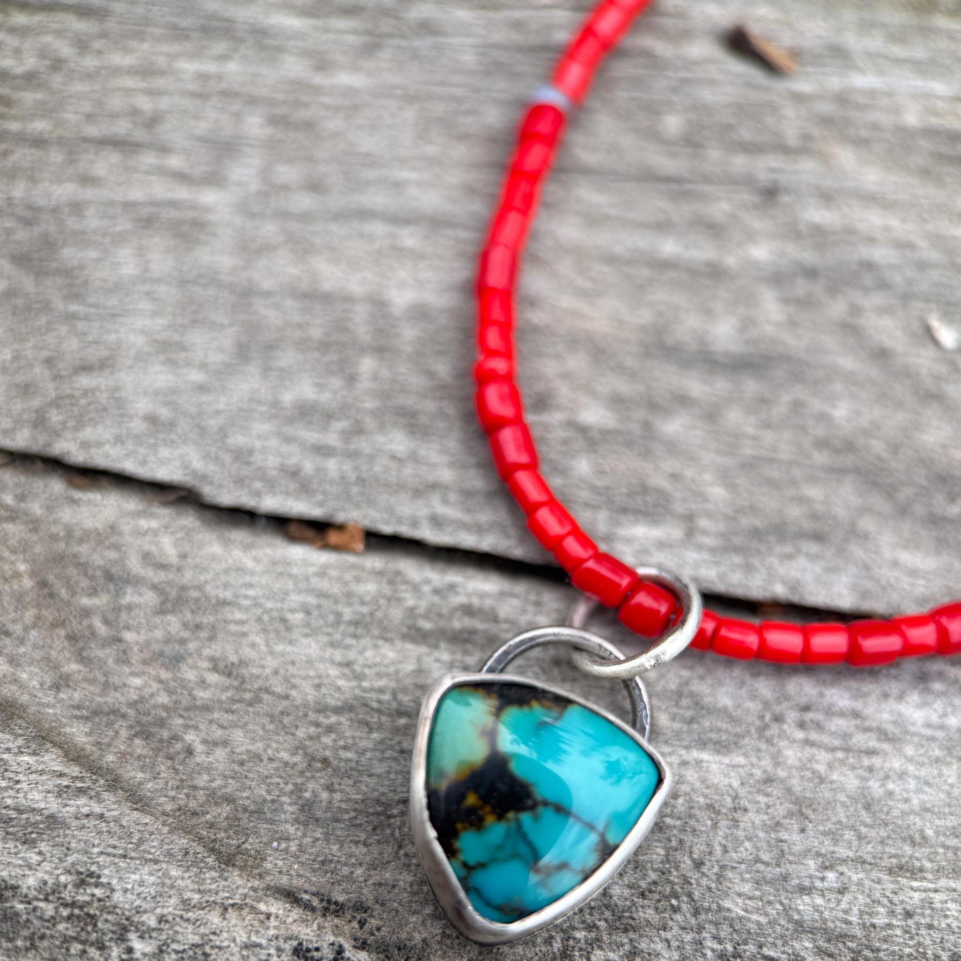 Necklace with turquoise pendant and red beads on a wooden surface