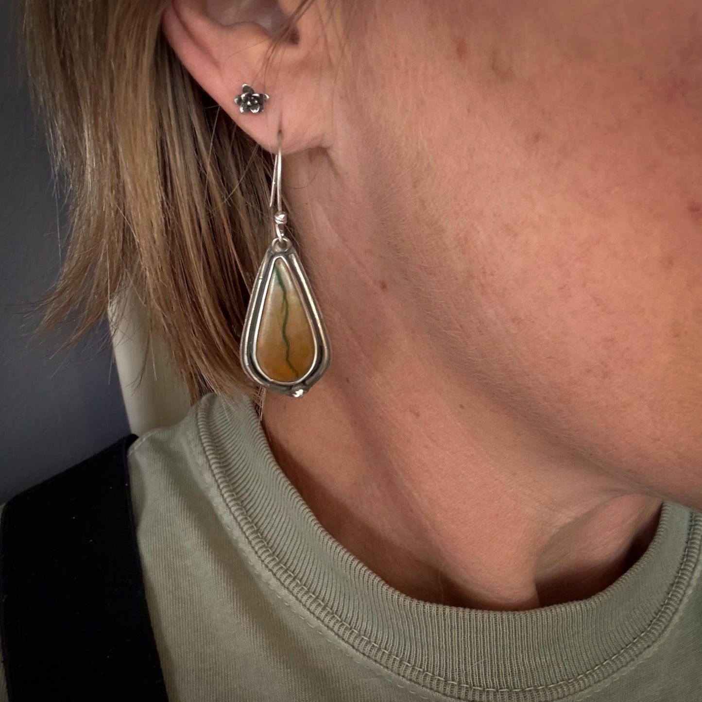 Close-up of a person wearing a teardrop-shaped earring with a green stone.