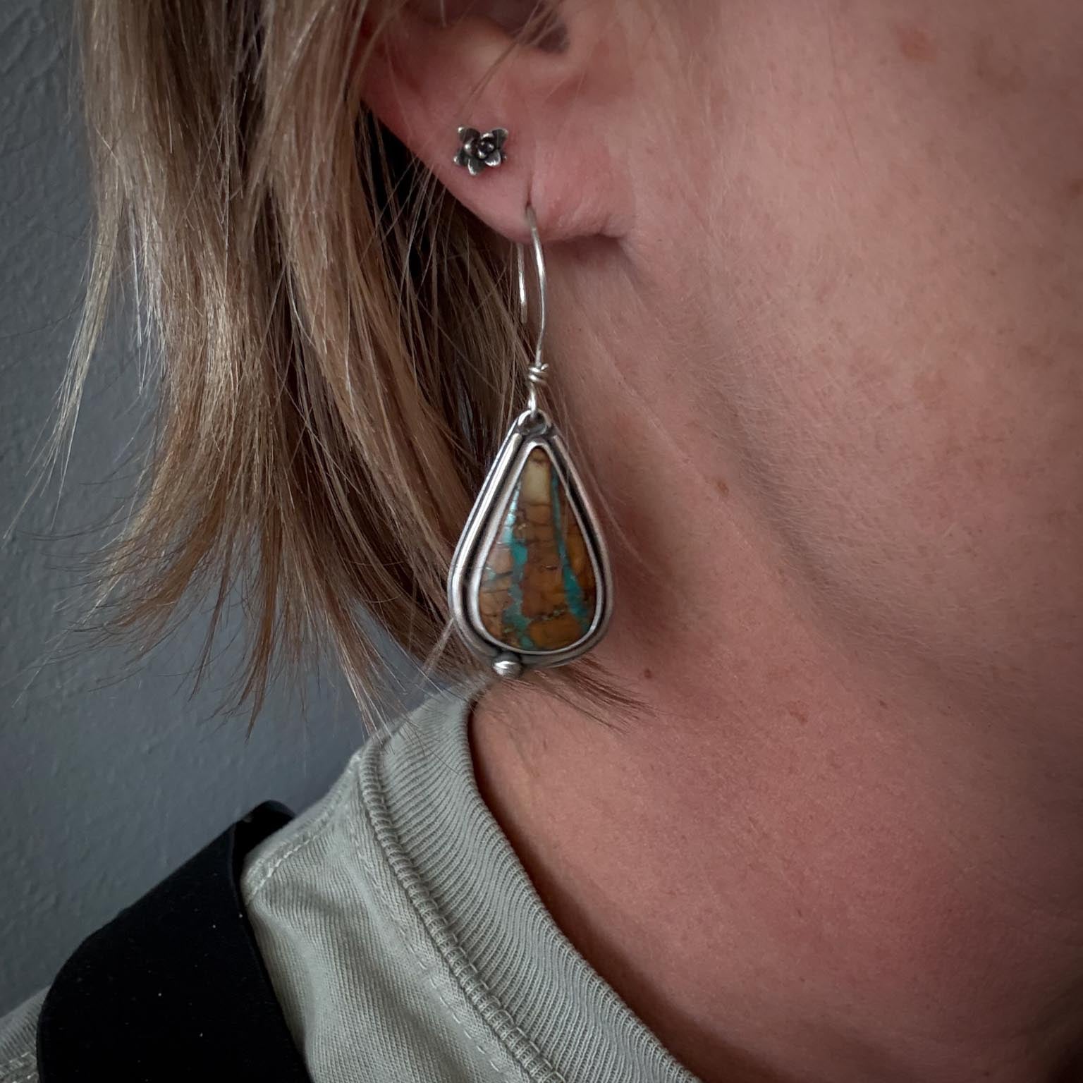 Close-up of a person wearing a silver earring with a turquoise stone.