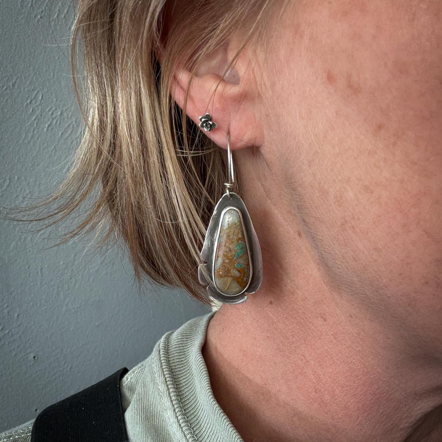 Close-up of a person wearing a silver earring with a stone pendant against a neutral background