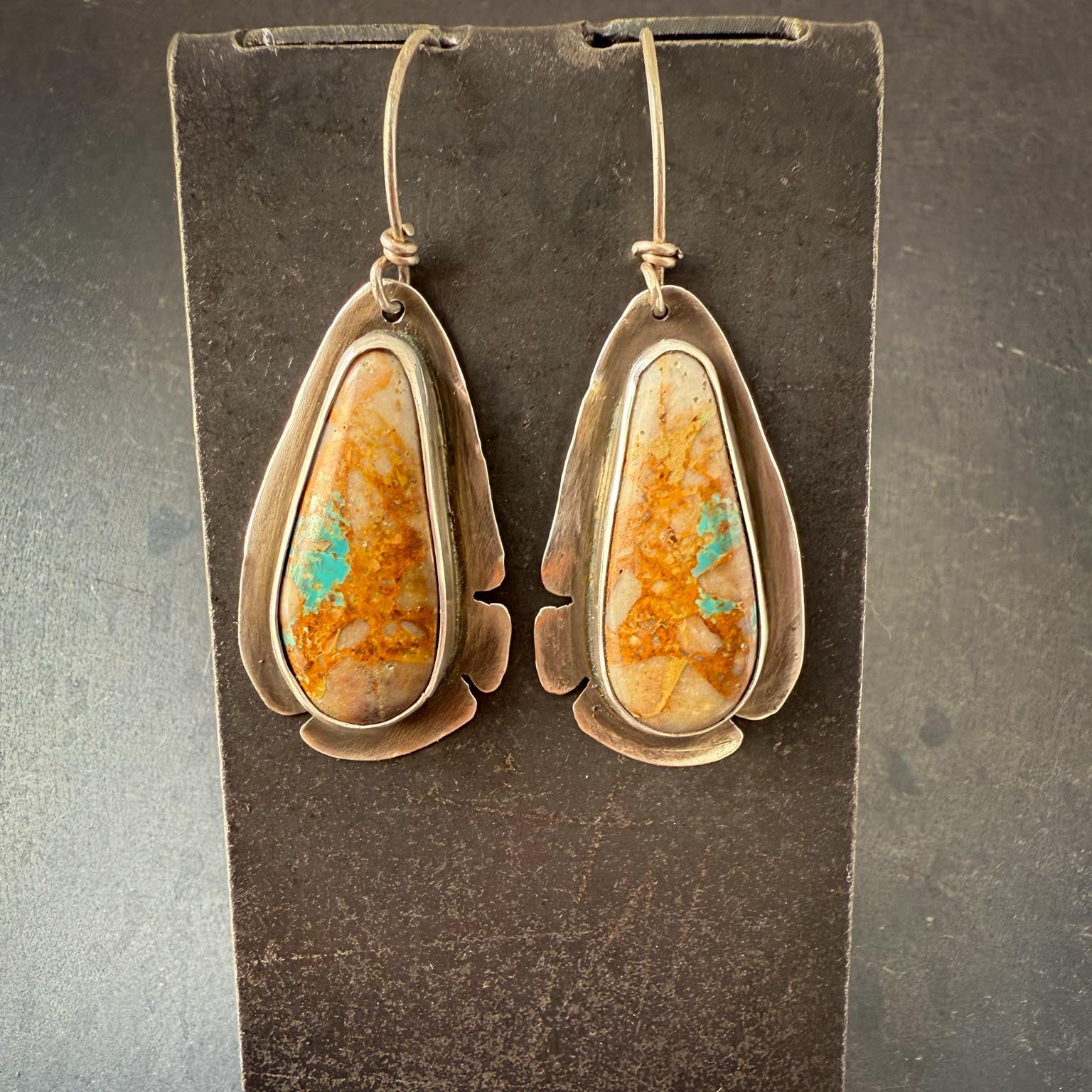 Pair of earrings with teardrop-shaped orange and green stones on a dark background