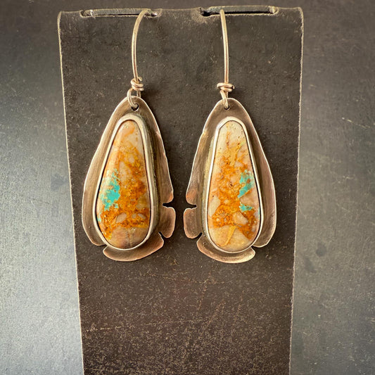 Pair of earrings with teardrop-shaped orange and green stones on a dark background