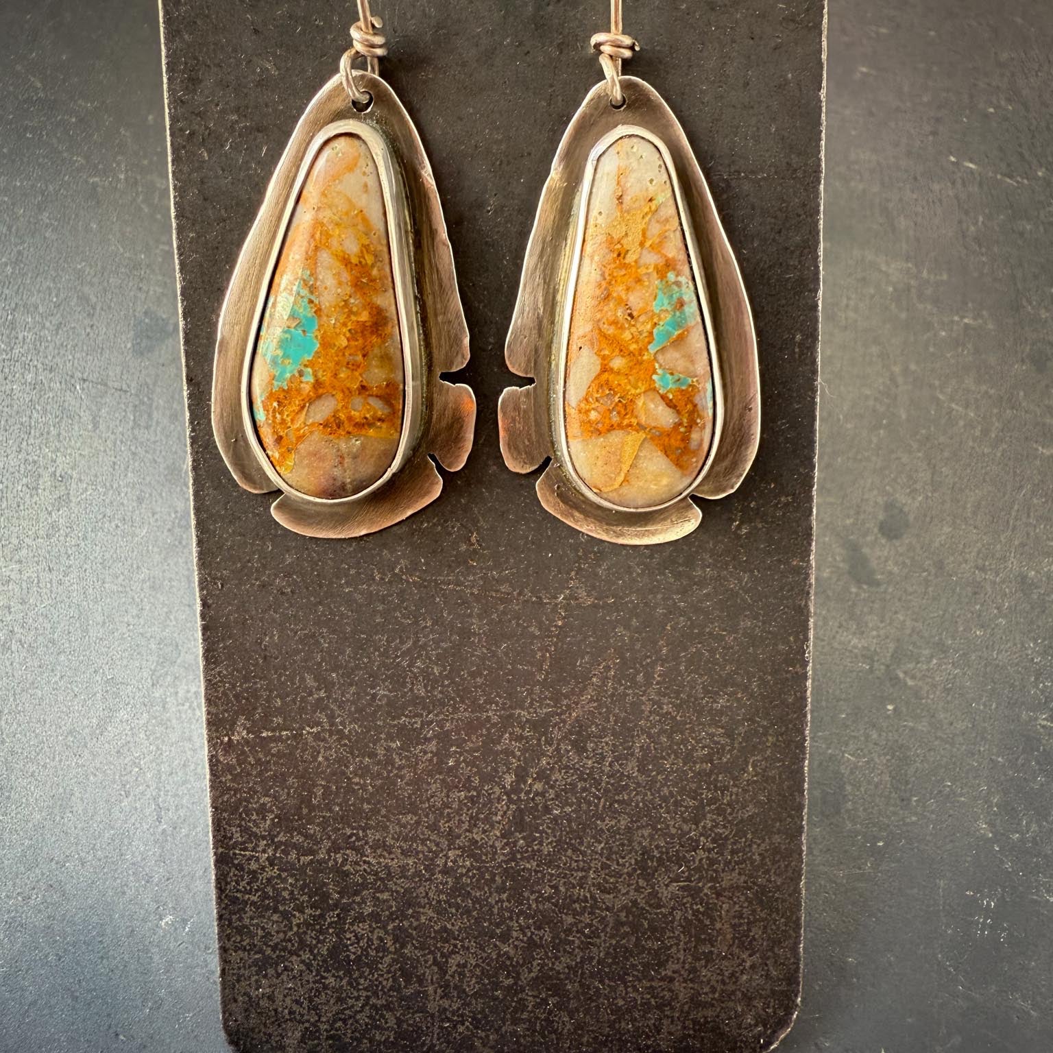 Pair of earrings with orange and green stone on a dark gray card