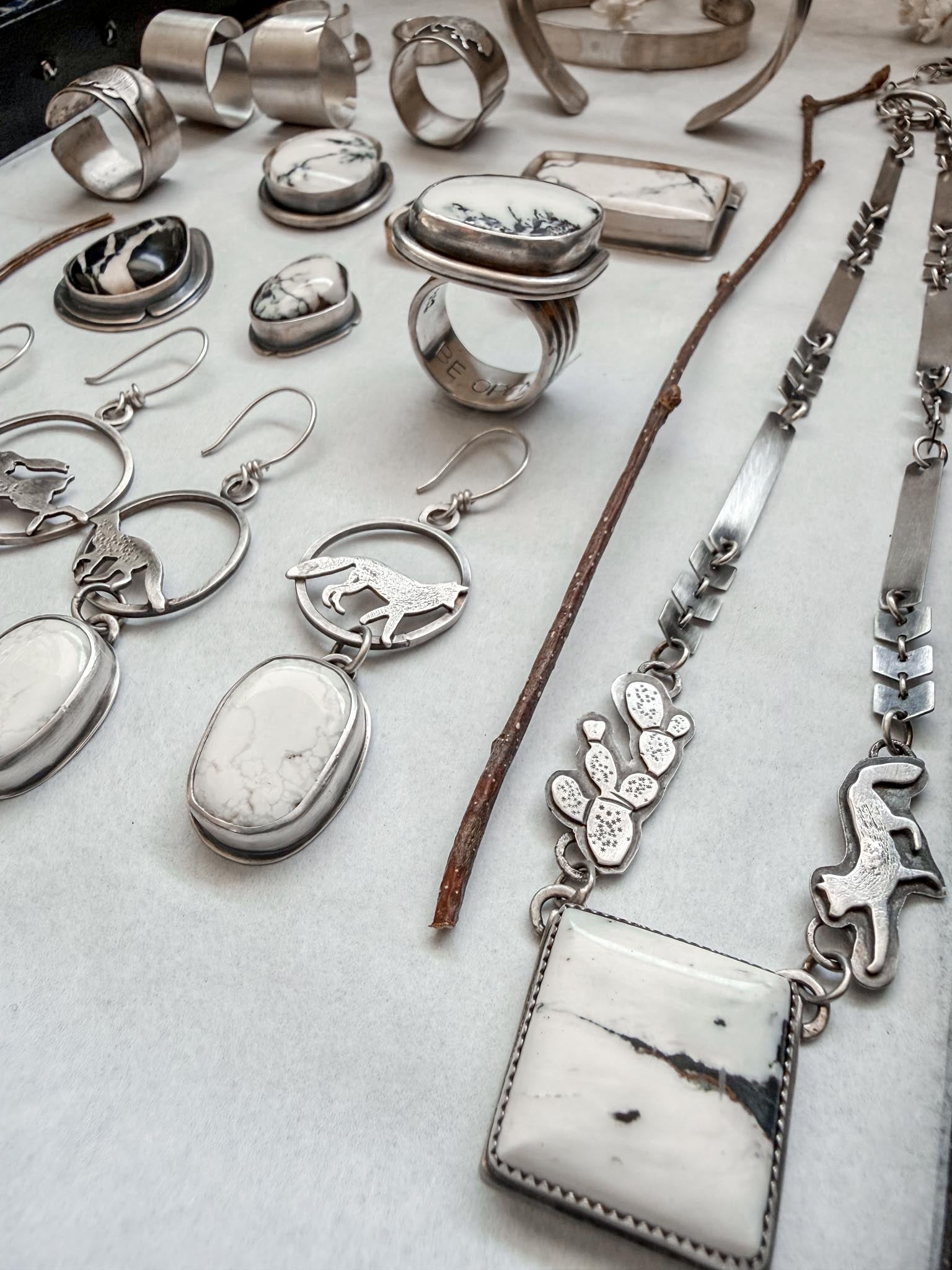 Collection of silver jewelry including rings, earrings, and a necklace on a light background
