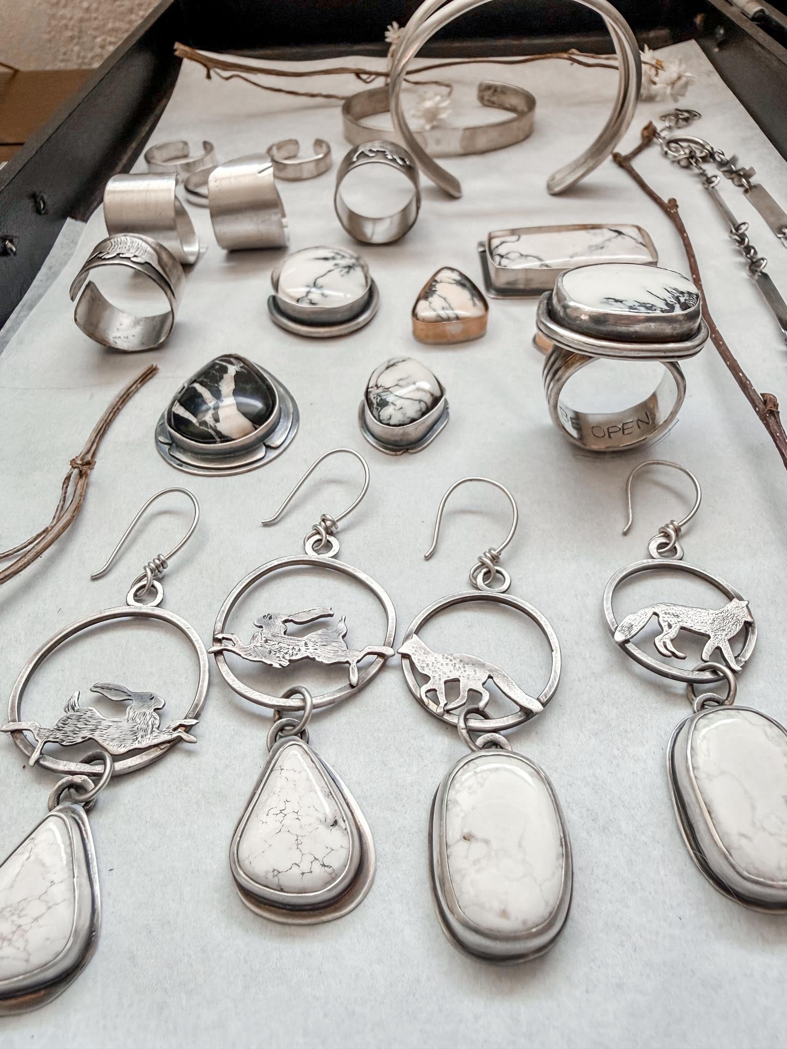 Collection of silver jewelry including rings, earrings, and necklaces on a white surface.
