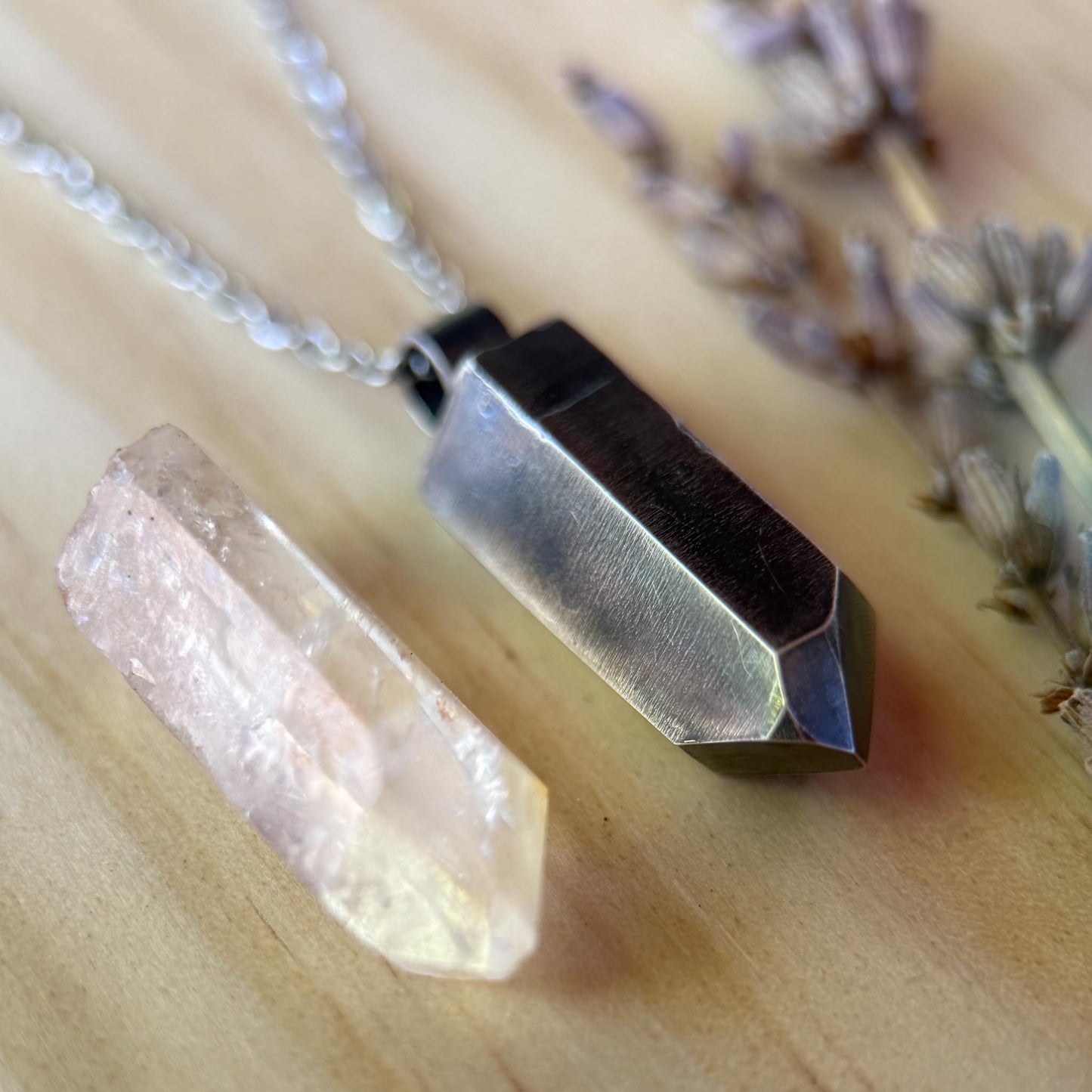 Necklace with geometric pendant and crystal on a wooden surface with lavender flowers.