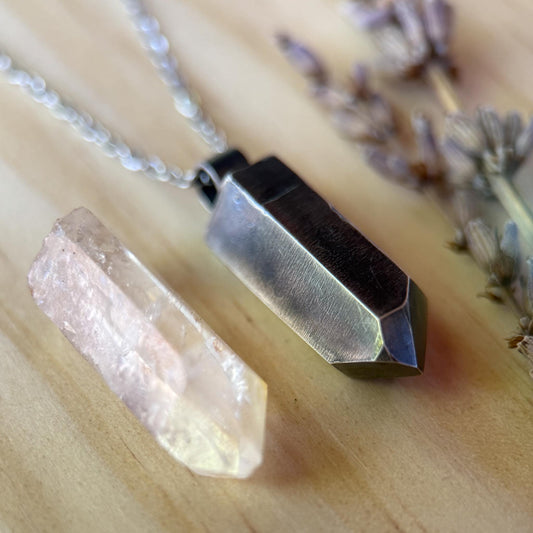 Necklace with geometric pendant and crystal on a wooden surface with lavender flowers.