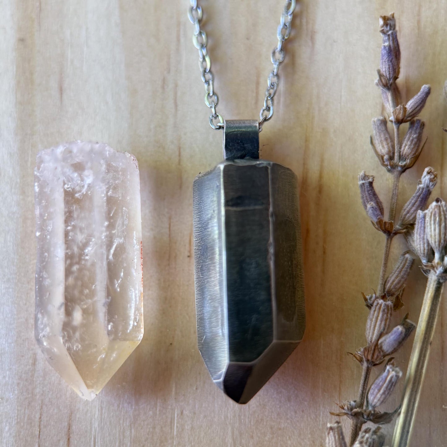 Crystal pendant necklace on a wooden surface with a crystal and dried lavender.