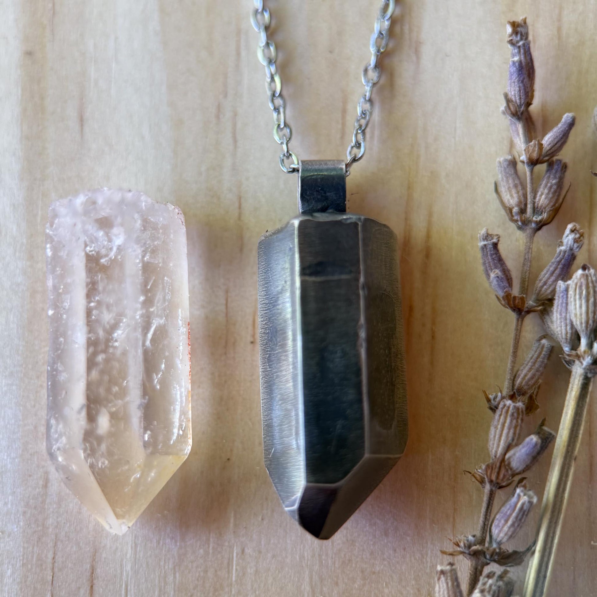 Crystal pendant necklace on a wooden surface with a crystal and dried lavender.