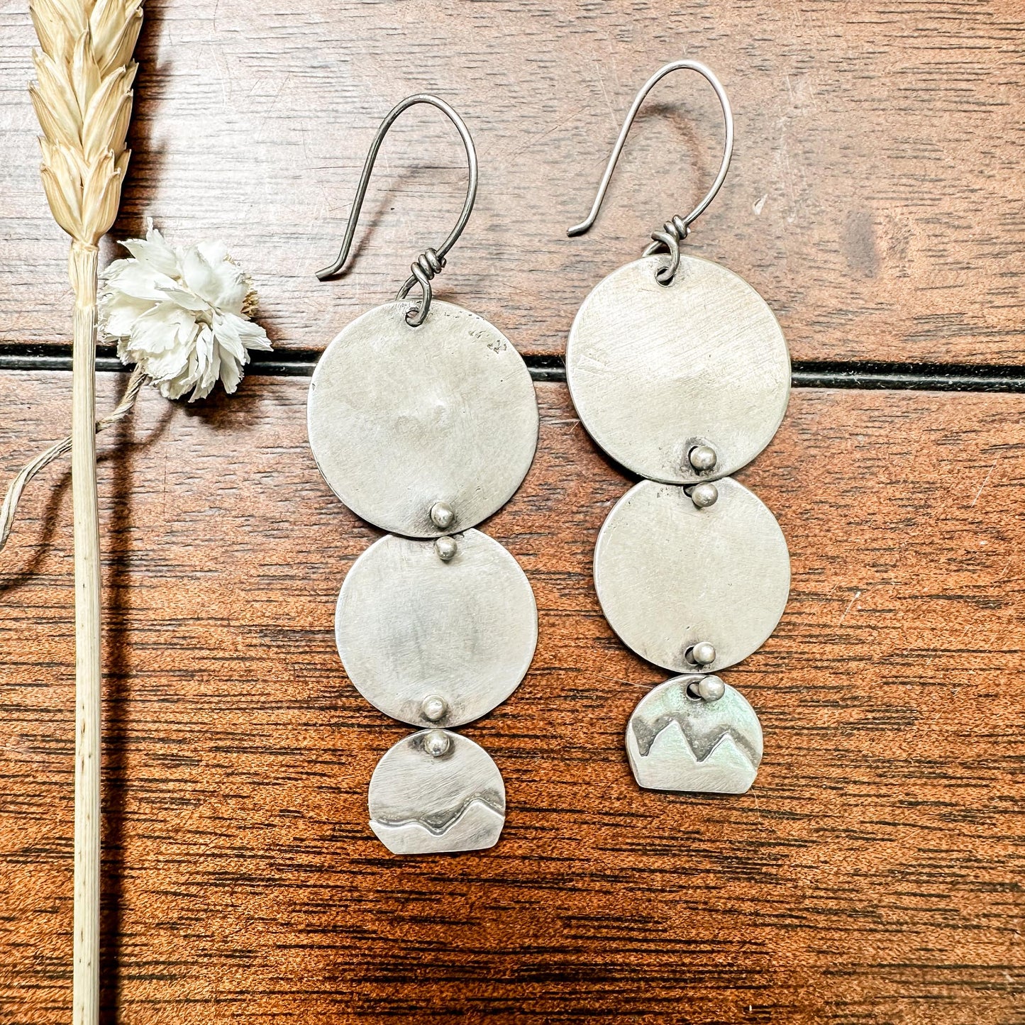 Three silver discs, each one smaller than the one above it are connected by silver pins, curved and soldered at the ends to allow movement and swing. The smaller disc dawns a small hand-fabricated mountain range. Oxidized to highlight the range. Lightweight and versatile. 