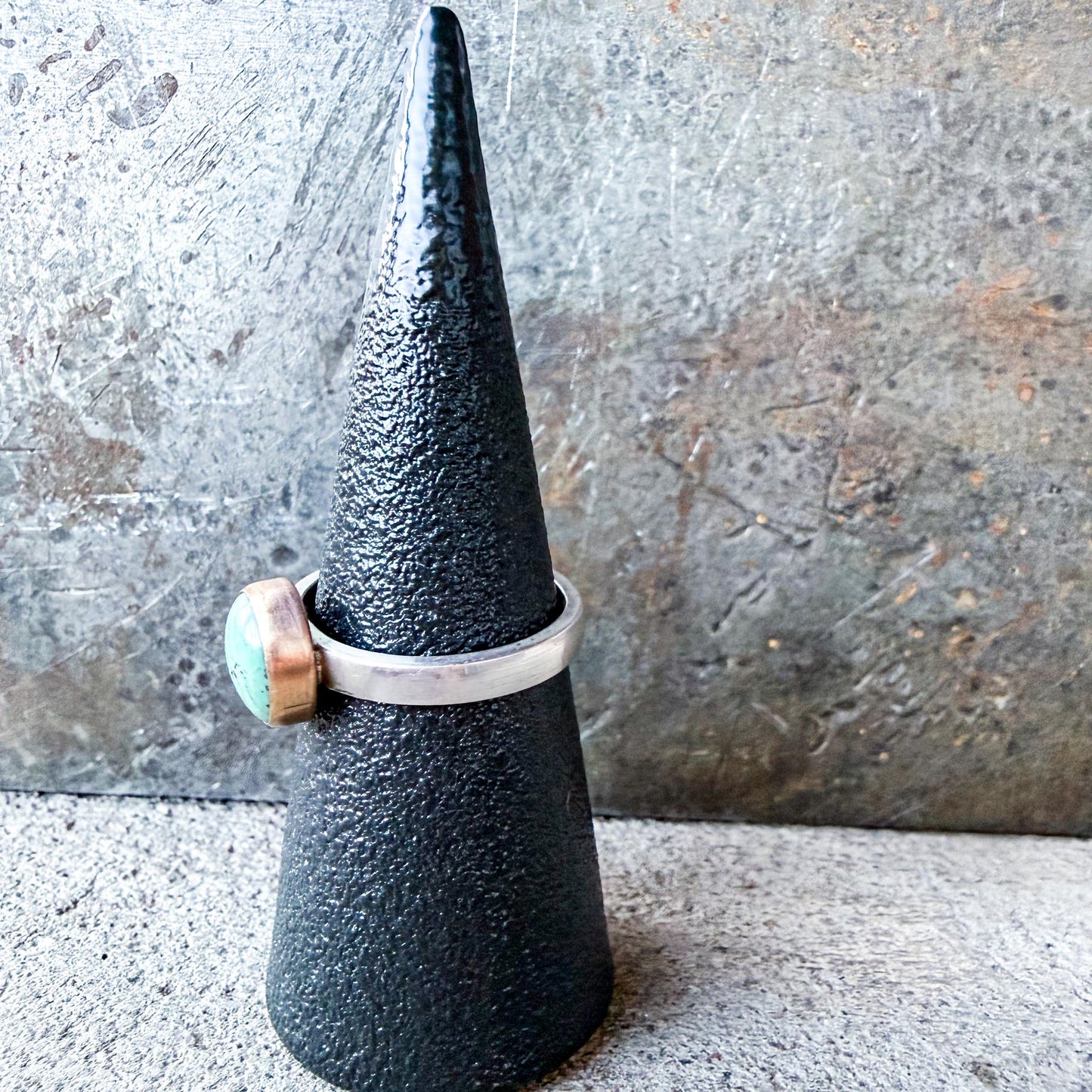 Silver ring with a turquoise stone on a textured black cone against a gray background