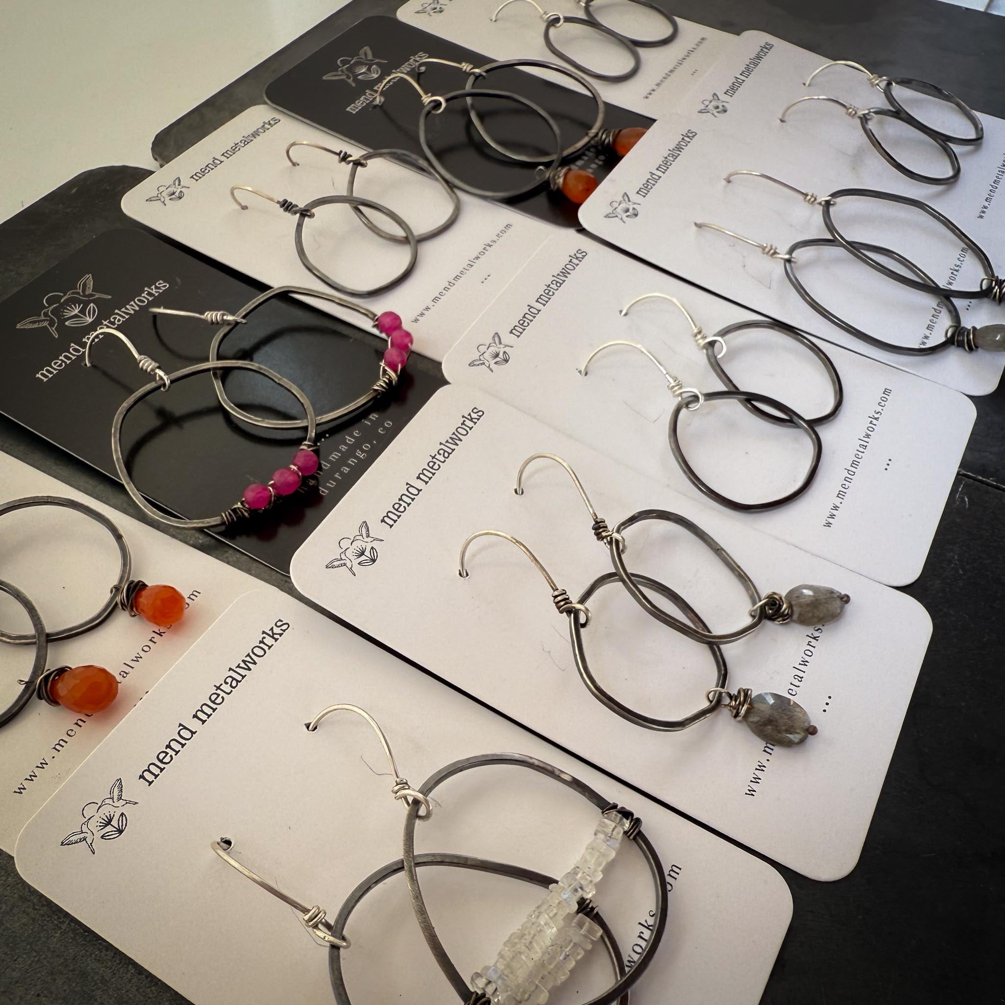Collection of earrings on display cards with 'mend metalworks' branding.