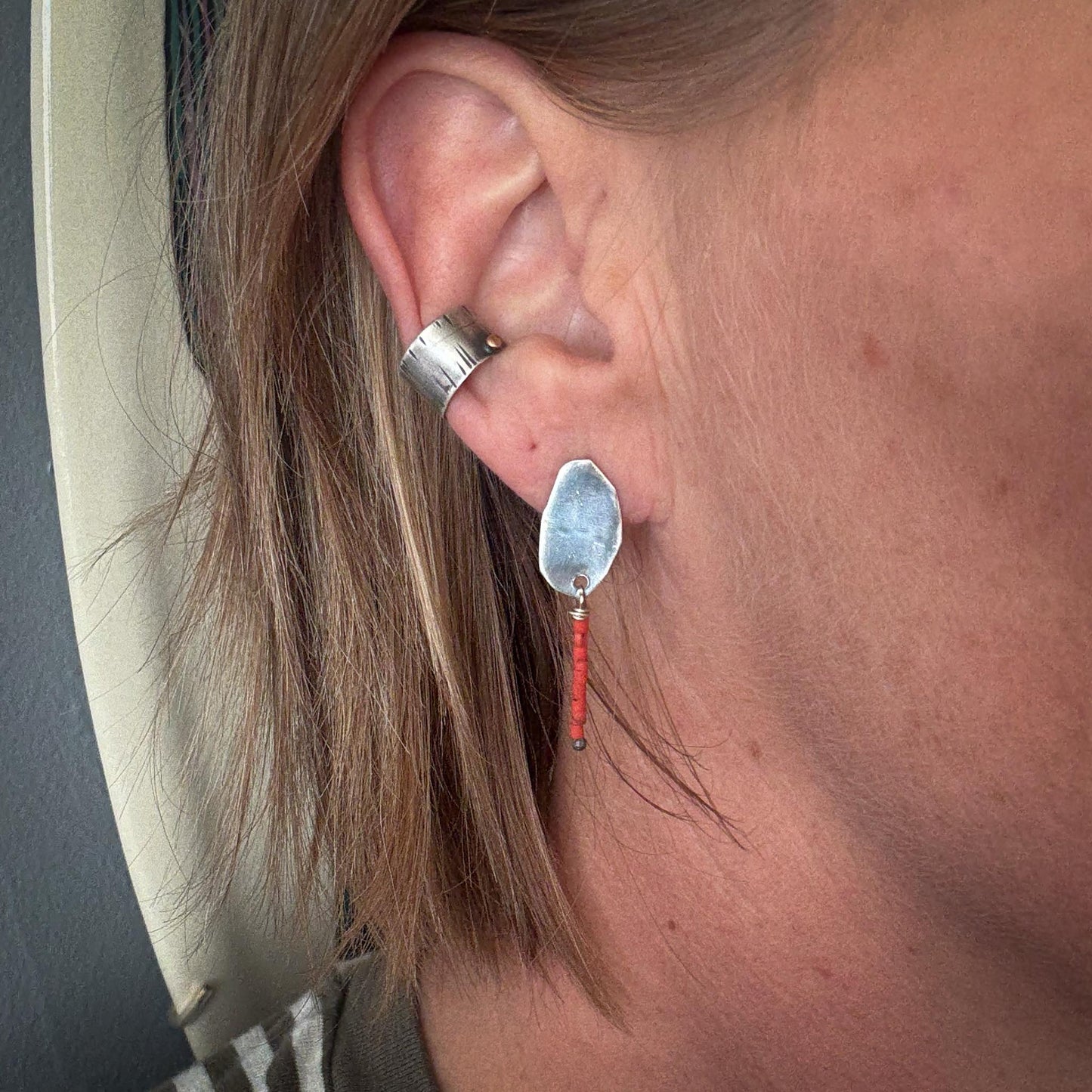 Close-up of an ear wearing a silver ring and a unique earring with a red bead.