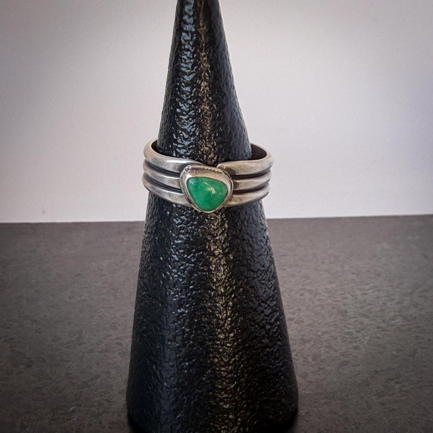 Silver ring with a green stone on a black cone-shaped object against a gray background