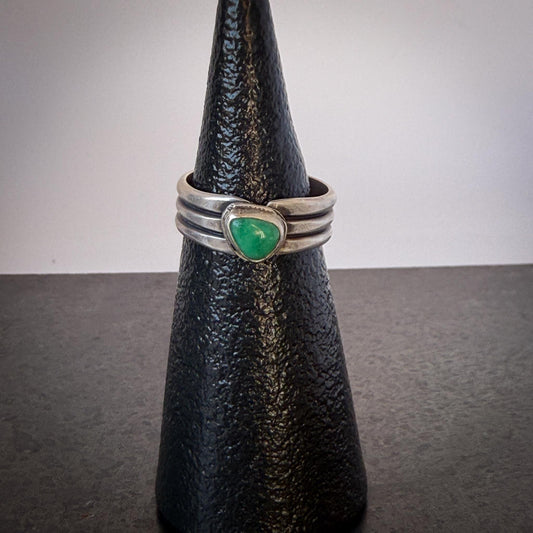 Silver ring with a green stone on a black cone-shaped object against a gray background