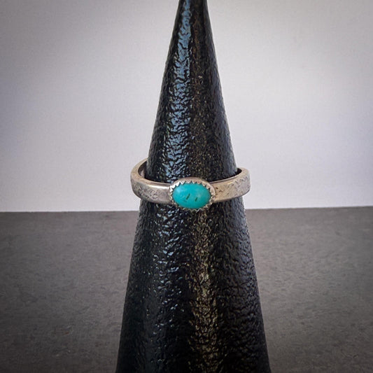 Silver ring with a turquoise stone on a black cone against a gray background