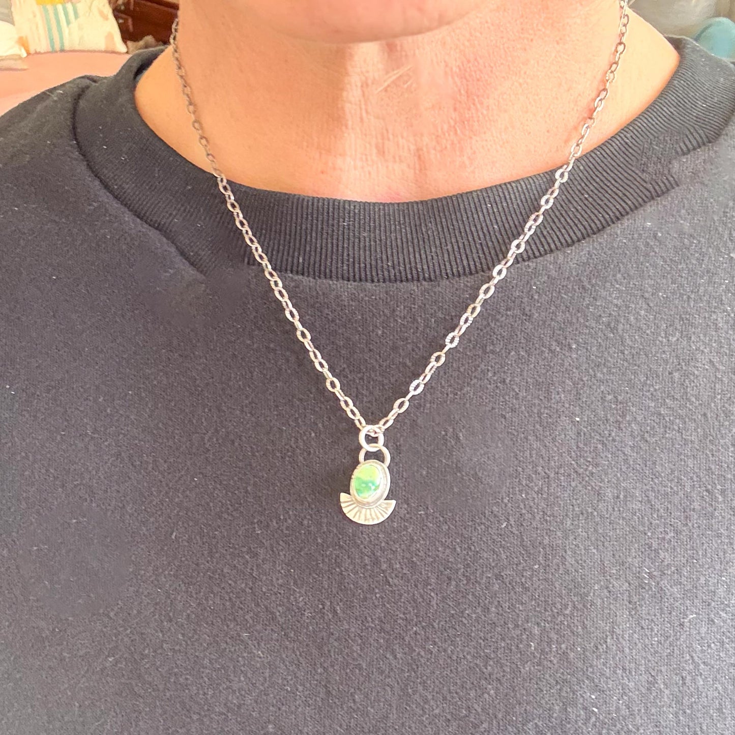 Person wearing a silver necklace with a pendant on a plain background