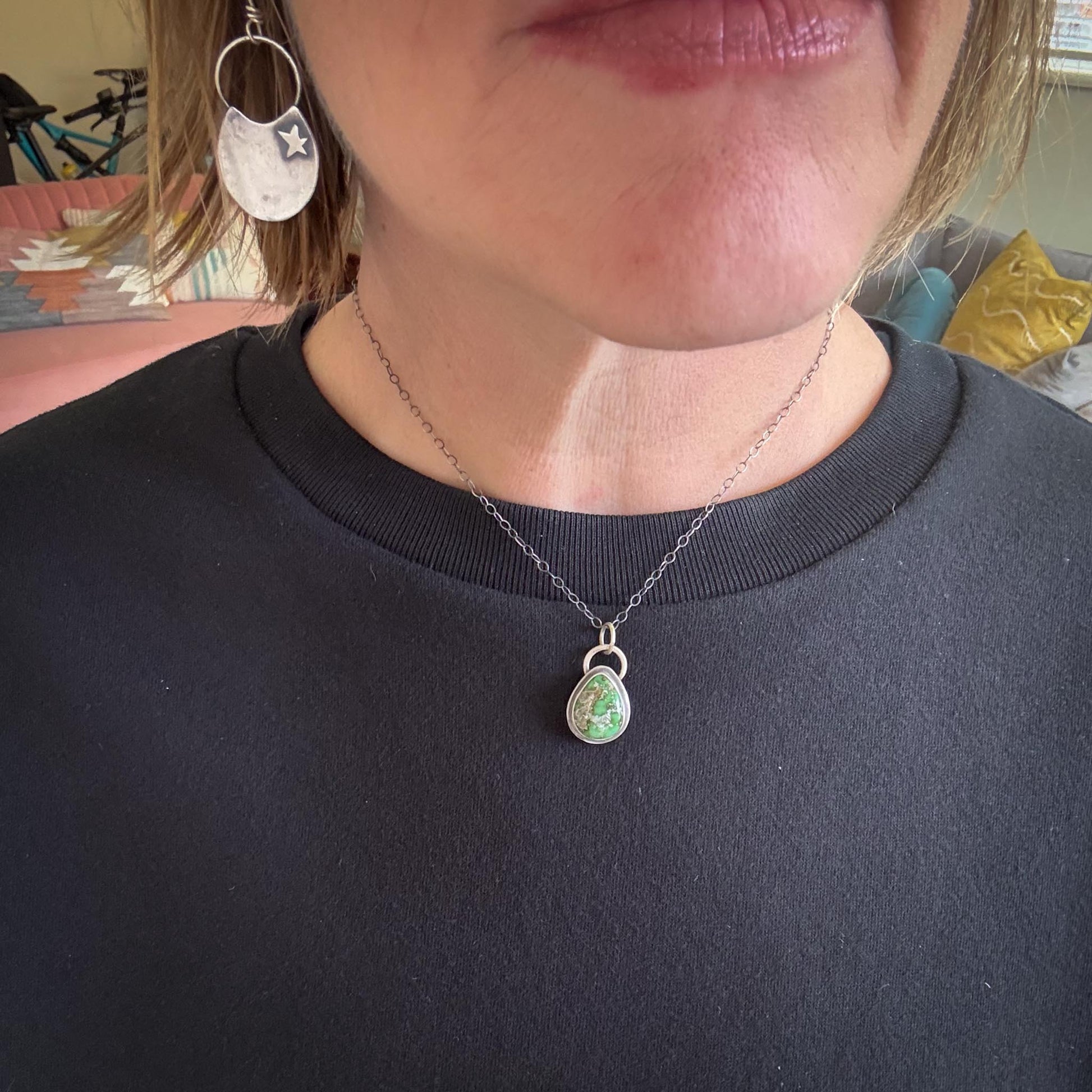 Person wearing a necklace with a pendant, indoors.